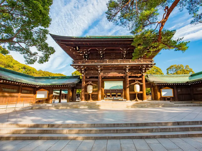 Gepflasterter Vorhof des stillen Meiji-Schreins in Tokio mit Blick auf das traditionelle, hölzerne Haupttor bei Sonnenschein.