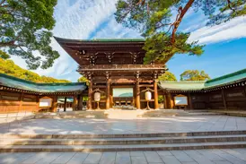 Gepflasterter Vorhof des stillen Meiji-Schreins in Tokio mit Blick auf das traditionelle, hölzerne Haupttor bei Sonnenschein.
