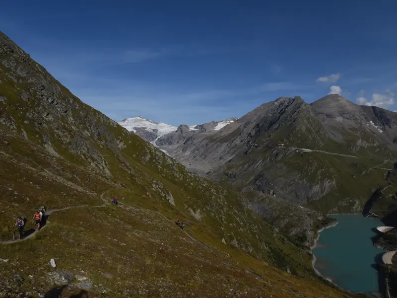 Trekkinggruppe auf einem aussichtsreichen Panoramasteig im Nationalpark Hohe Tauern mit Blick auf einen Stausee und Gletscher.