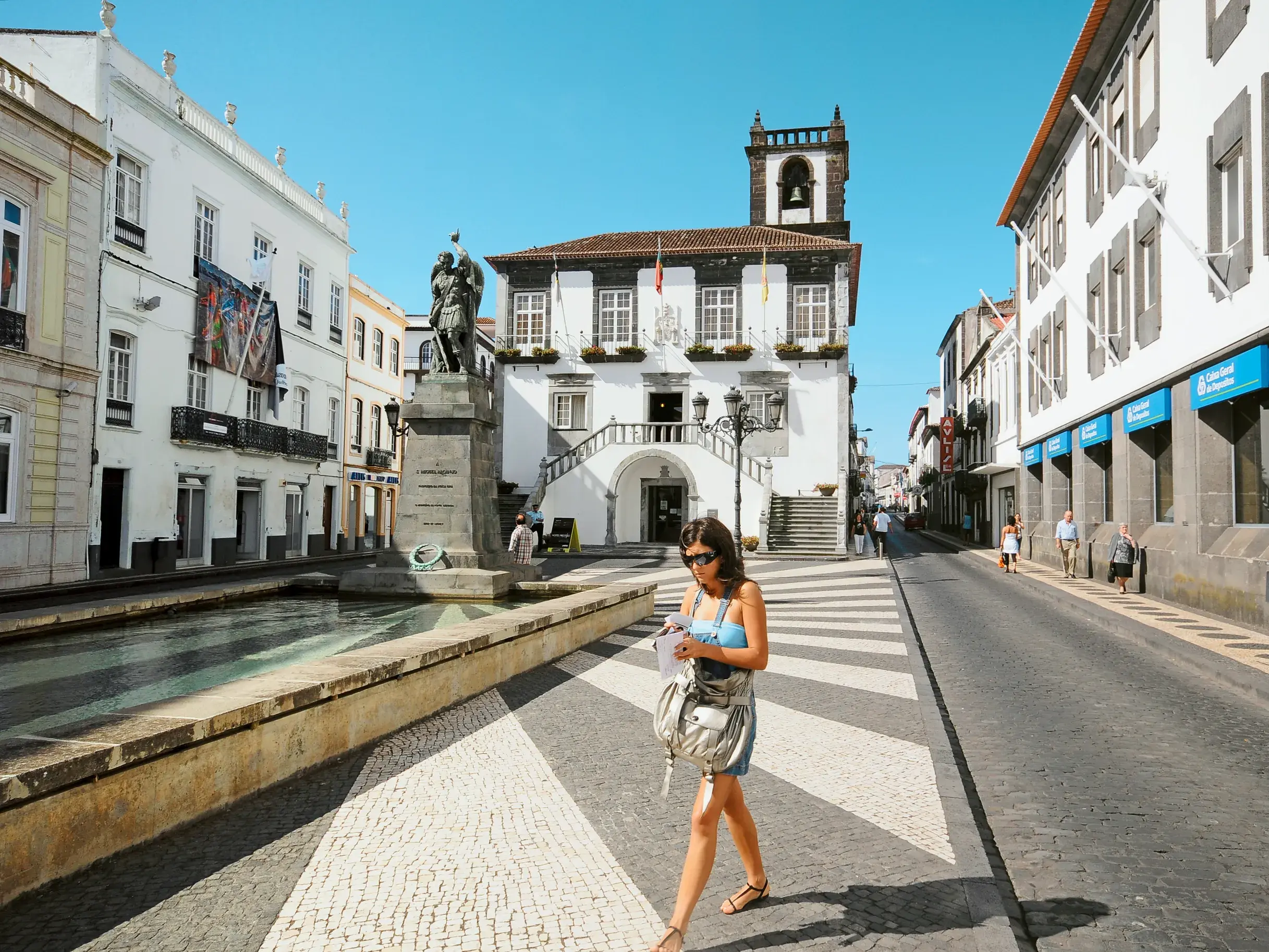 Eine Frau erkundet die Altstadt von Ponta Delgada mit ihren typischen schwarz-weiß gemusterten Straßen und historischen Gebäuden.
