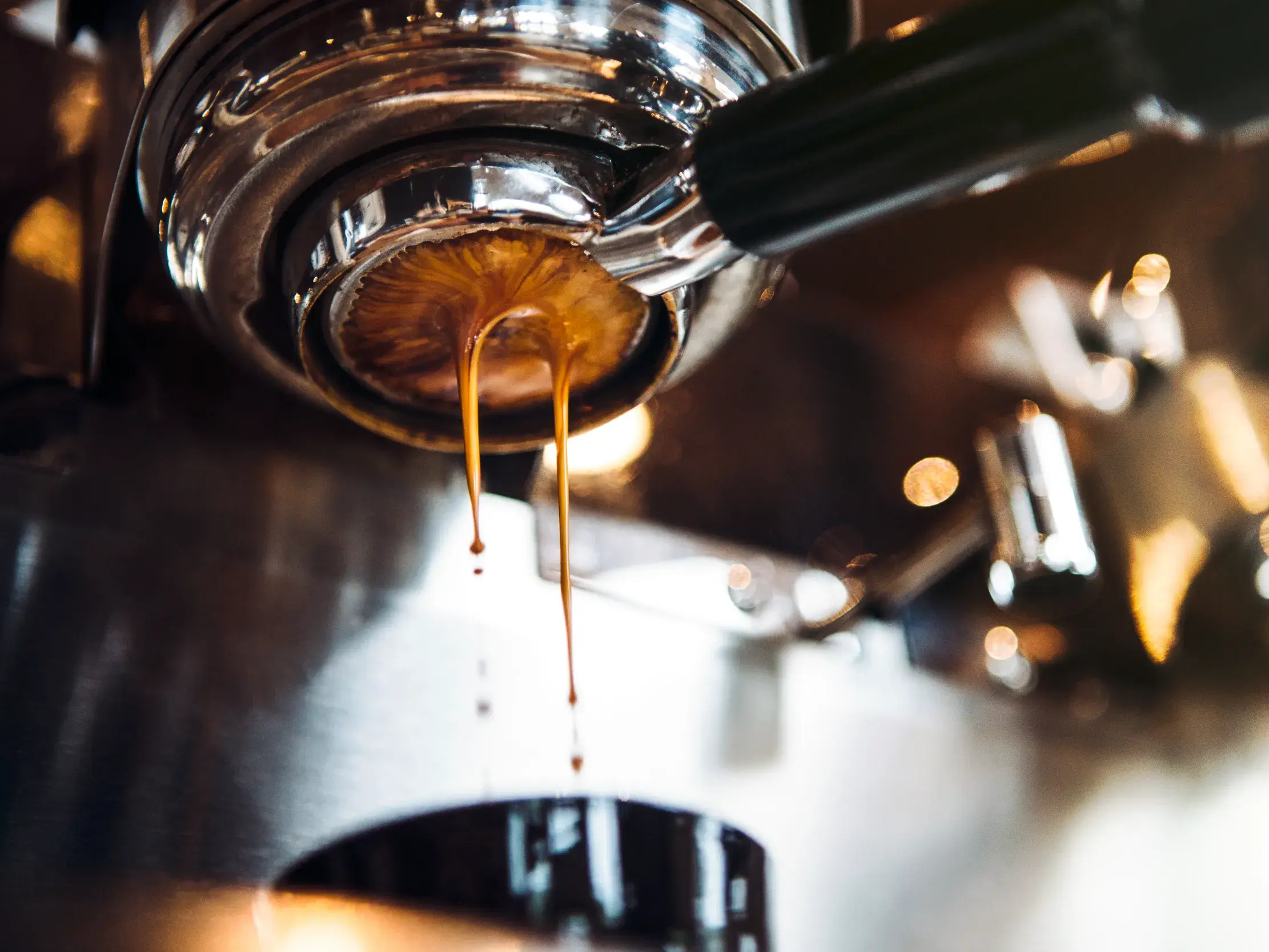 Nahaufnahme von frisch gebrühtem Espresso, der aus dem Siebträger einer Chrom-Kaffeemaschine in einem italienischen Café rinnt.