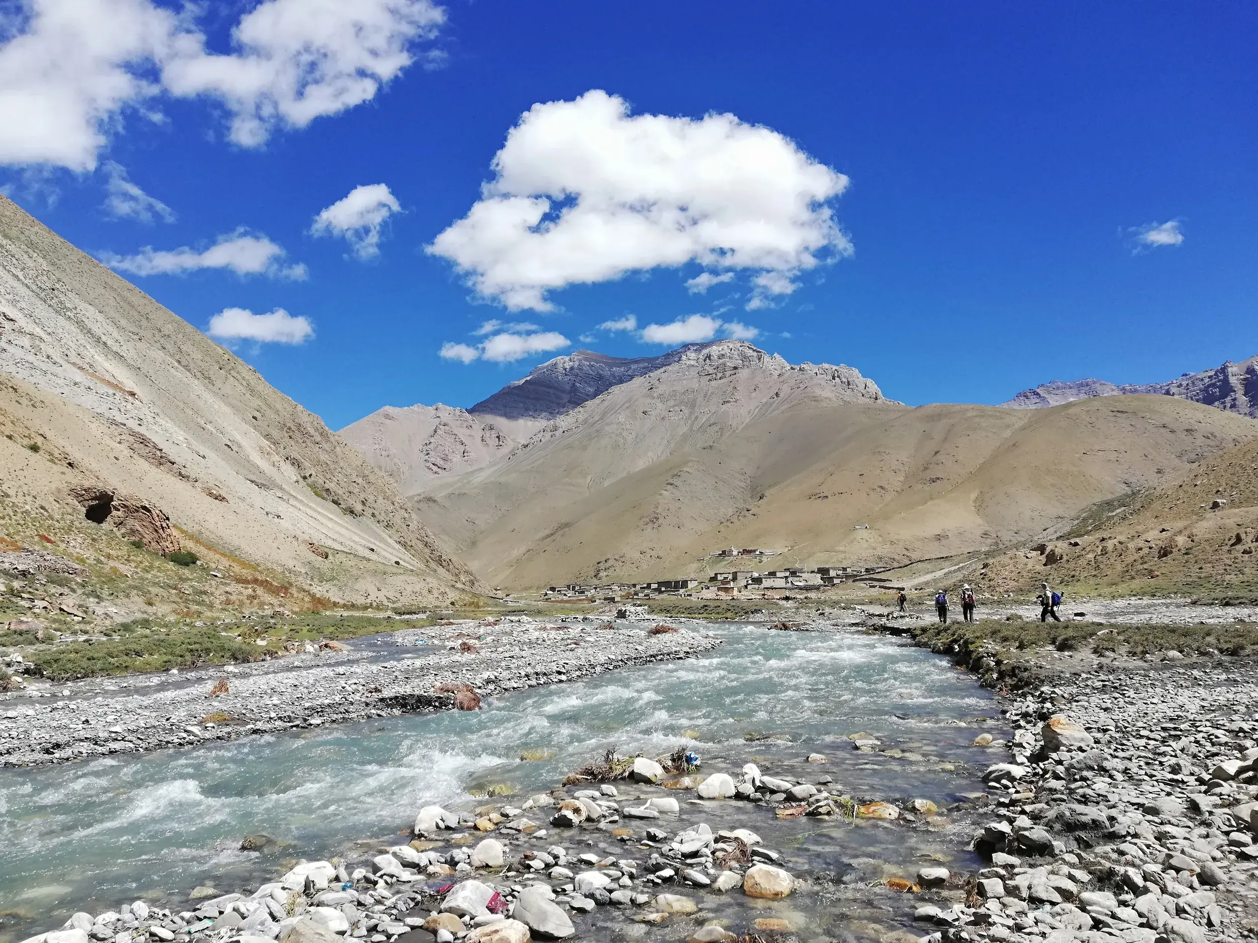 Eine kleine Wandergruppe beim Trekking am Fluss Tarap Khola in einem weiten, kargen Tal der Dolpo-Region in Nepal.