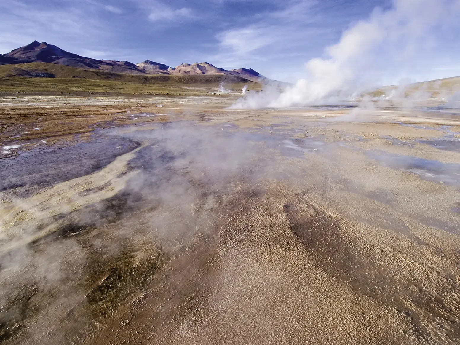 Dampf steigt aus den Geysiren von El Tatio im Altiplano auf, im Hintergrund die Bergkette der Anden in der Atacama-Wüste.