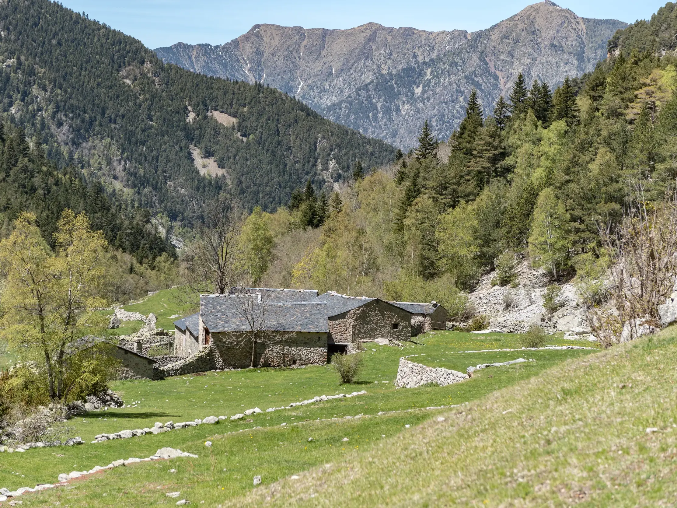 Traditionelle Almhütten aus Stein auf einer grünen Wiese im Madriu-Tal, dem UNESCO-Weltkulturerbe in den Pyrenäen Andorras.