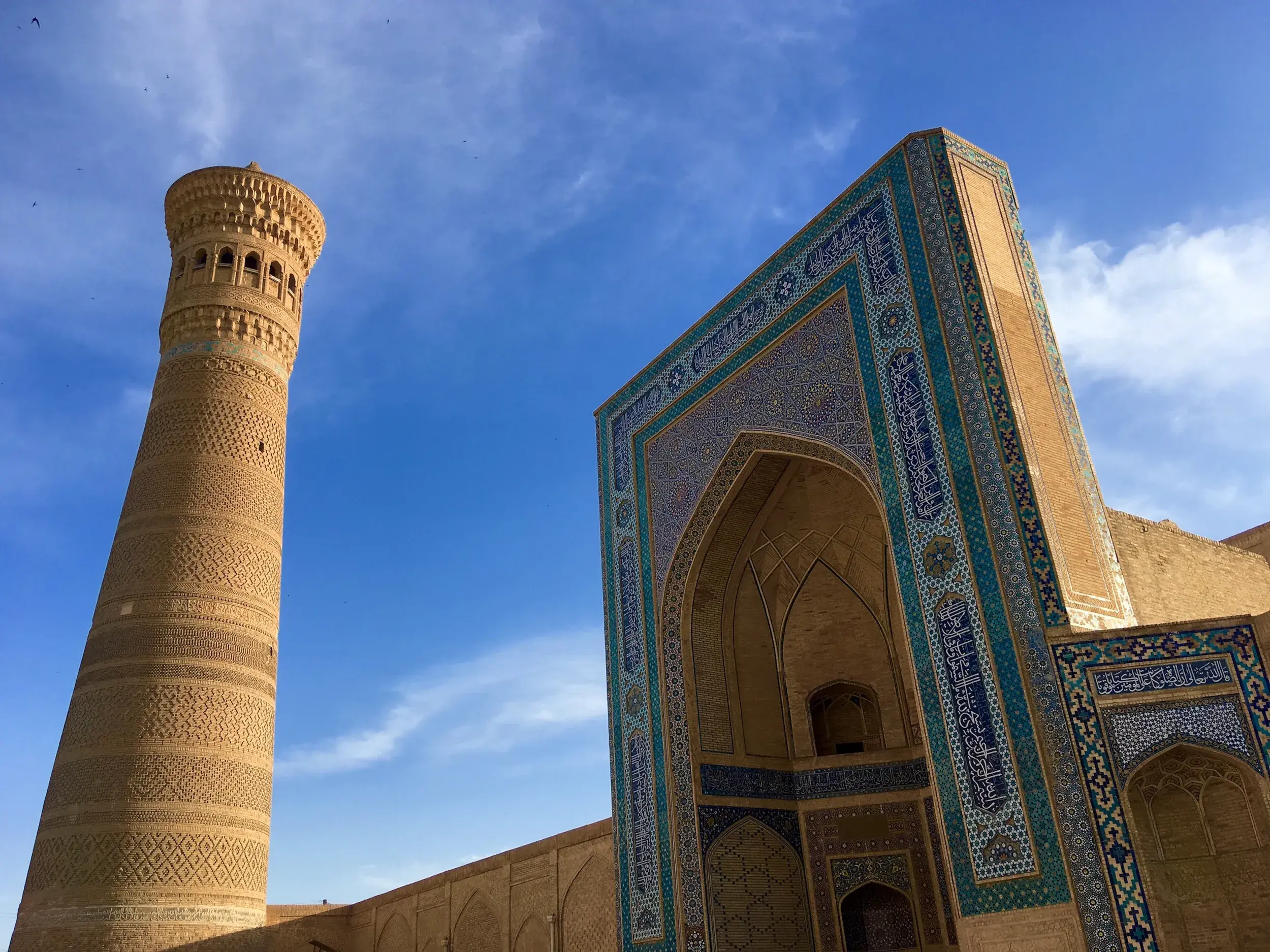 Blick auf das imposante Kalan-Minarett und das blaue Mosaik-Portal der Mir-i-Arab-Medrese in Buchara, Usbekistan.