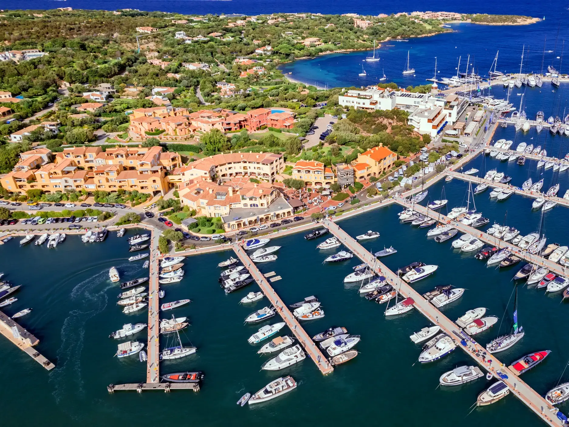 Luftaufnahme des mondänen Yachthafens von Porto Cervo an Sardiniens Costa Smeralda mit vielen Booten und Hotels am Ufer.