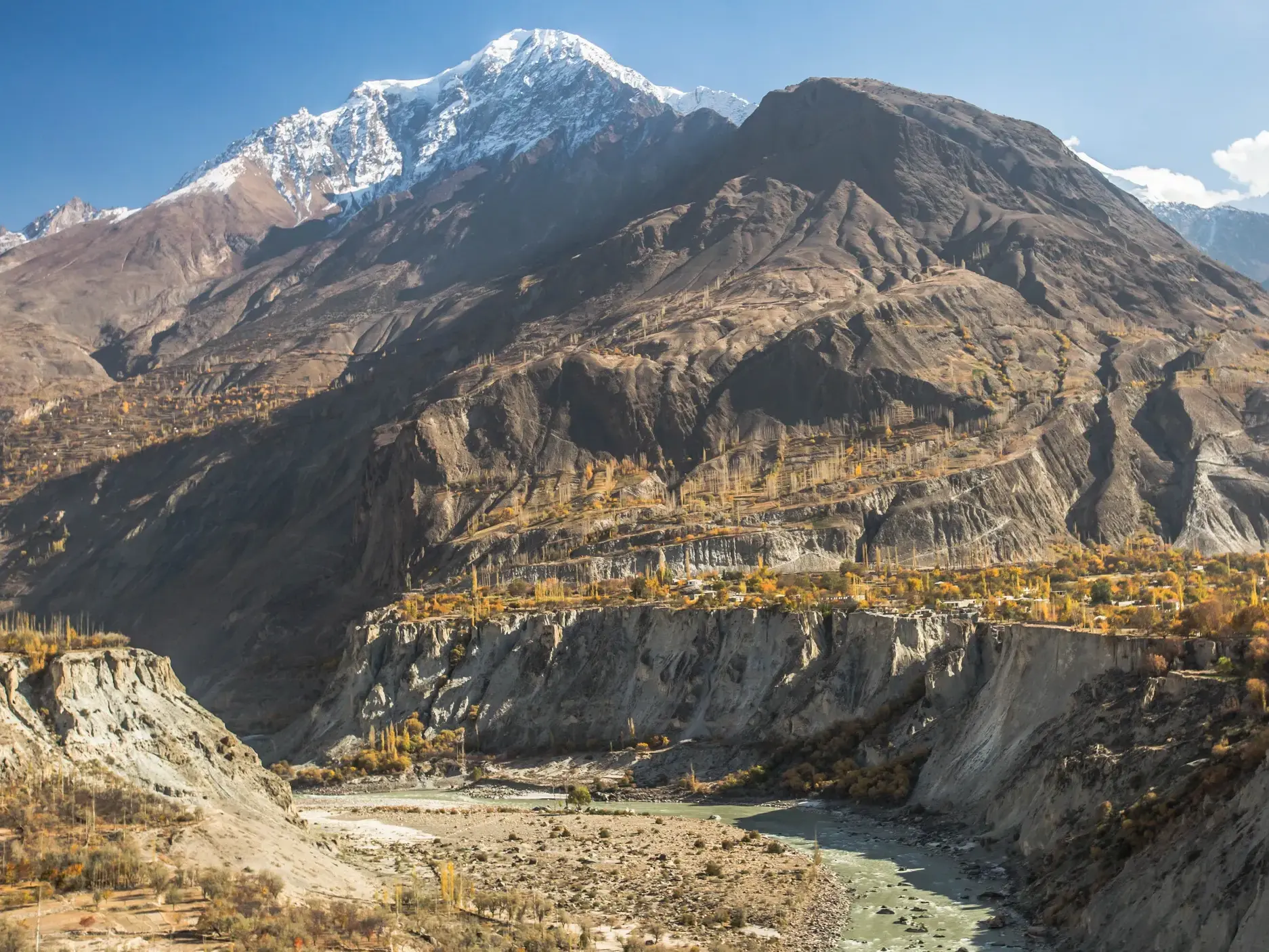 Majestätischer, schneebedeckter Rakaposhi-Gipfel über dem herbstlichen Hunzatal mit einem Flussbett in Nordpakistan.