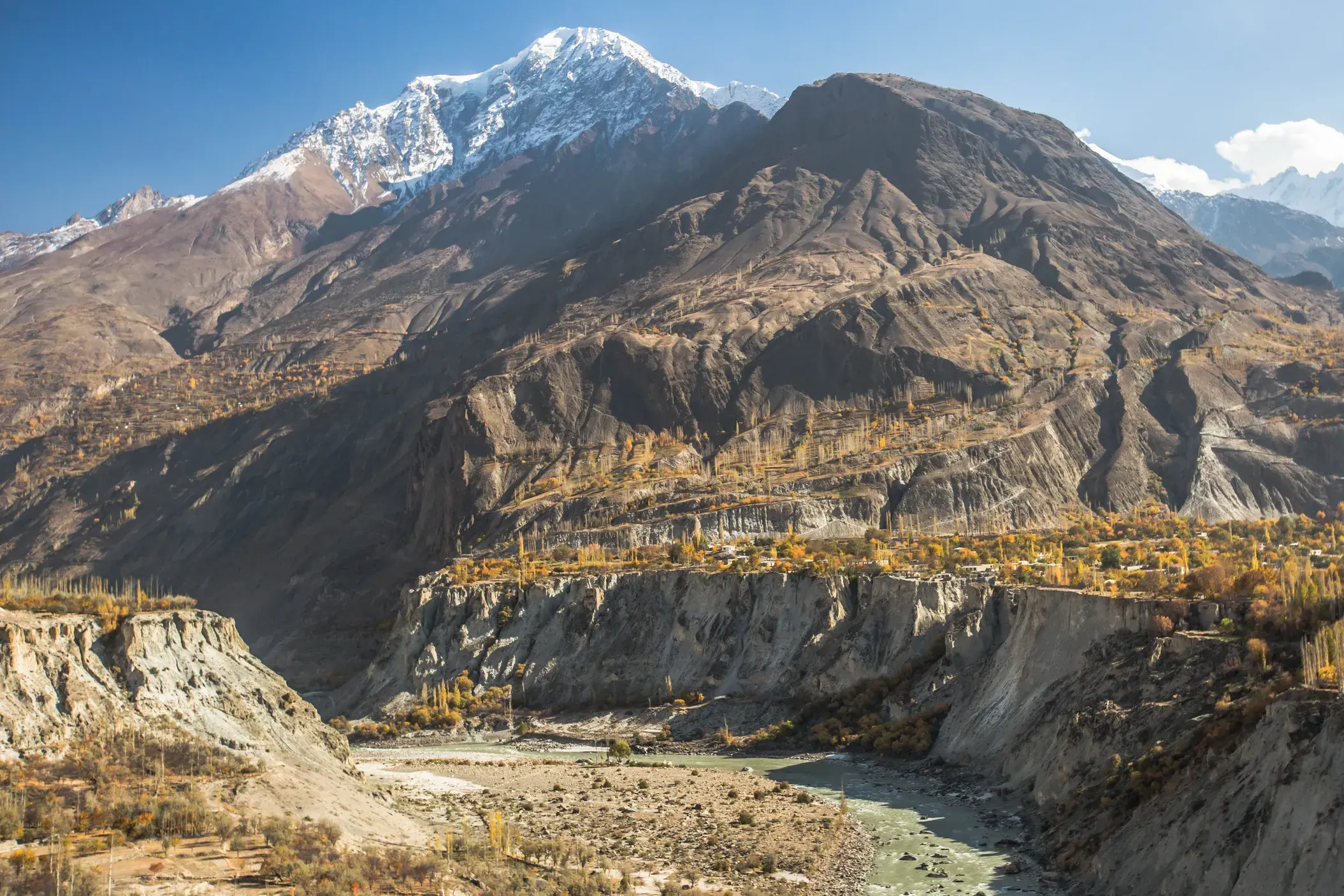Majestätischer, schneebedeckter Rakaposhi-Gipfel über dem herbstlichen Hunzatal mit einem Flussbett in Nordpakistan.