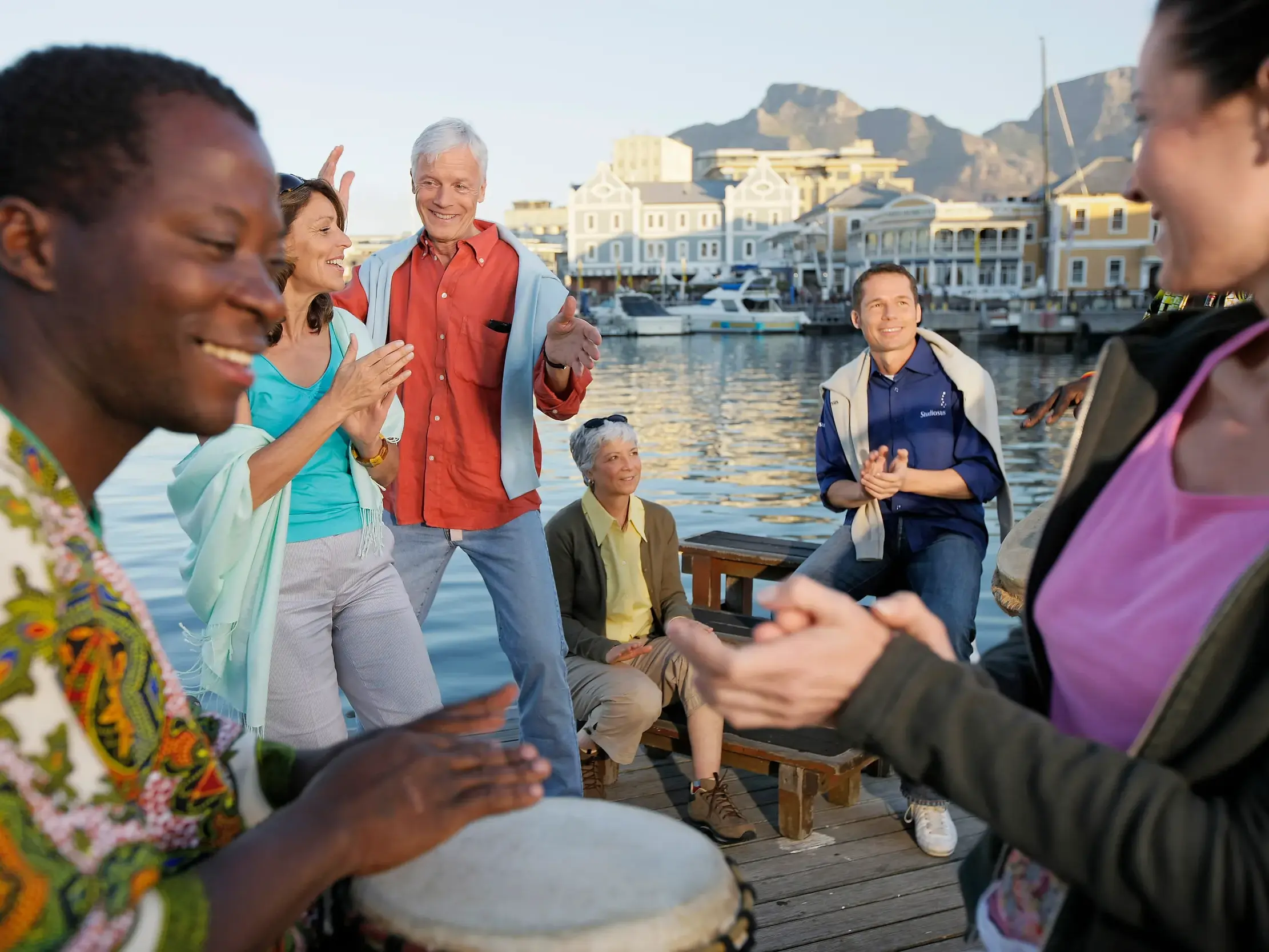 Einheimischer Musiker trommelt für eine fröhliche Studiosus Reisegruppe an der belebten V&A Waterfront in Kapstadt.