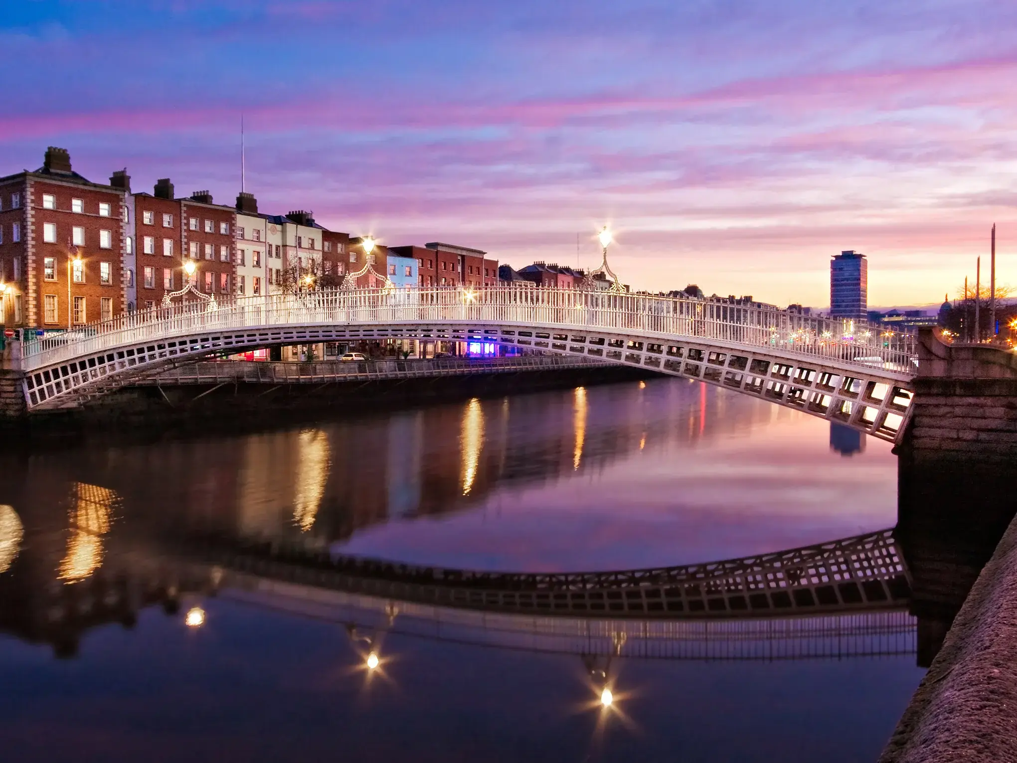 Stimmungsvolle Abenddämmerung in Dublin: Die beleuchtete Fußgängerbrücke über den Fluss Liffey spiegelt sich im Wasser.