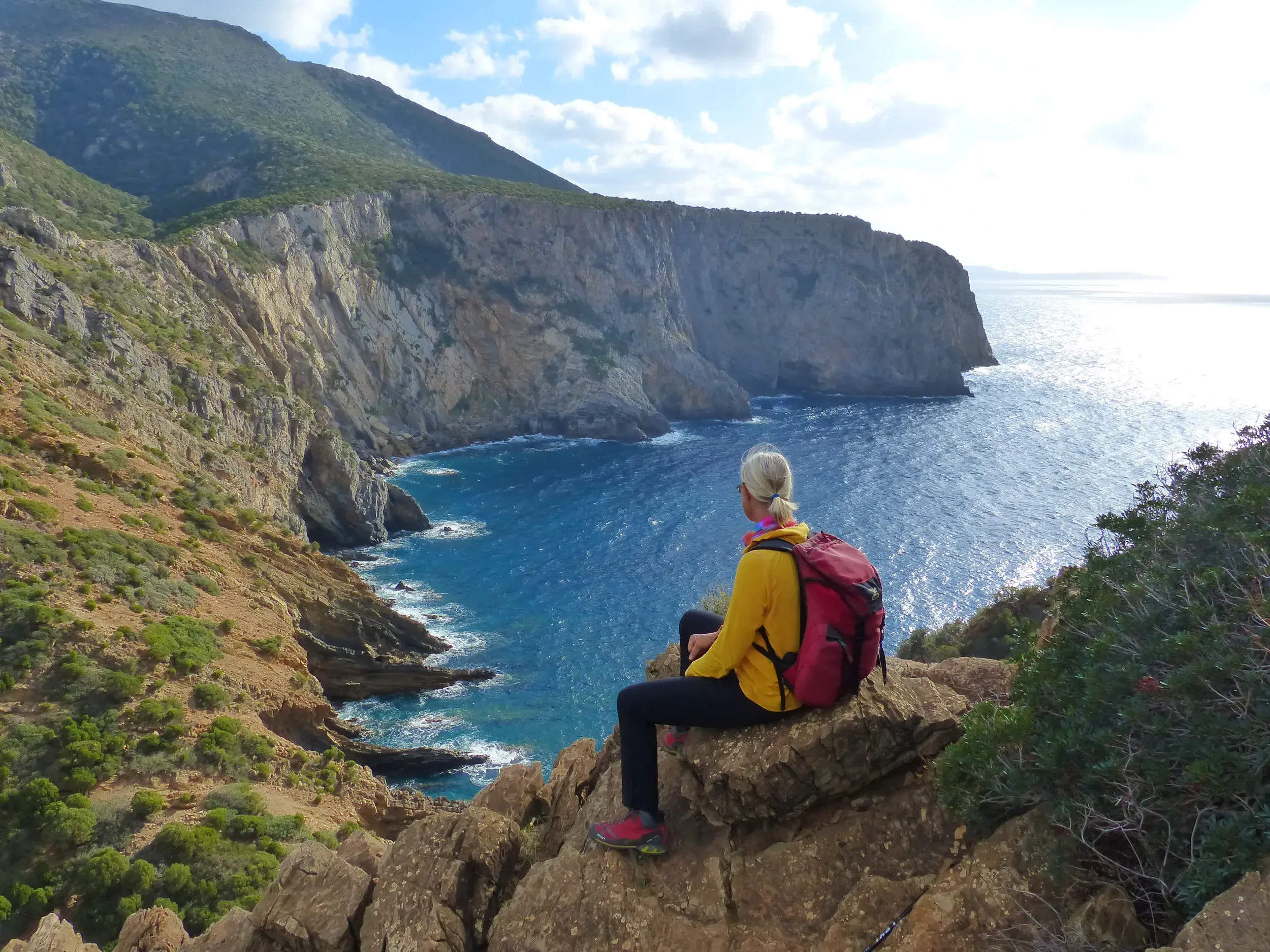 Wanderin macht eine Pause auf einem Felsen und blickt auf die Steilküste und das Meer bei Cala Domestica in Sardinien.