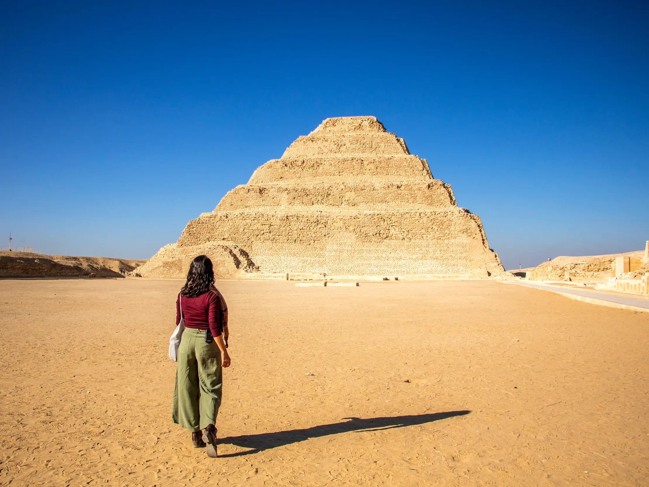 Teilnehmerin einer Studienreise geht durch den Wüstensand auf die imposante Stufenpyramide von Sakkara in Ägypten zu.