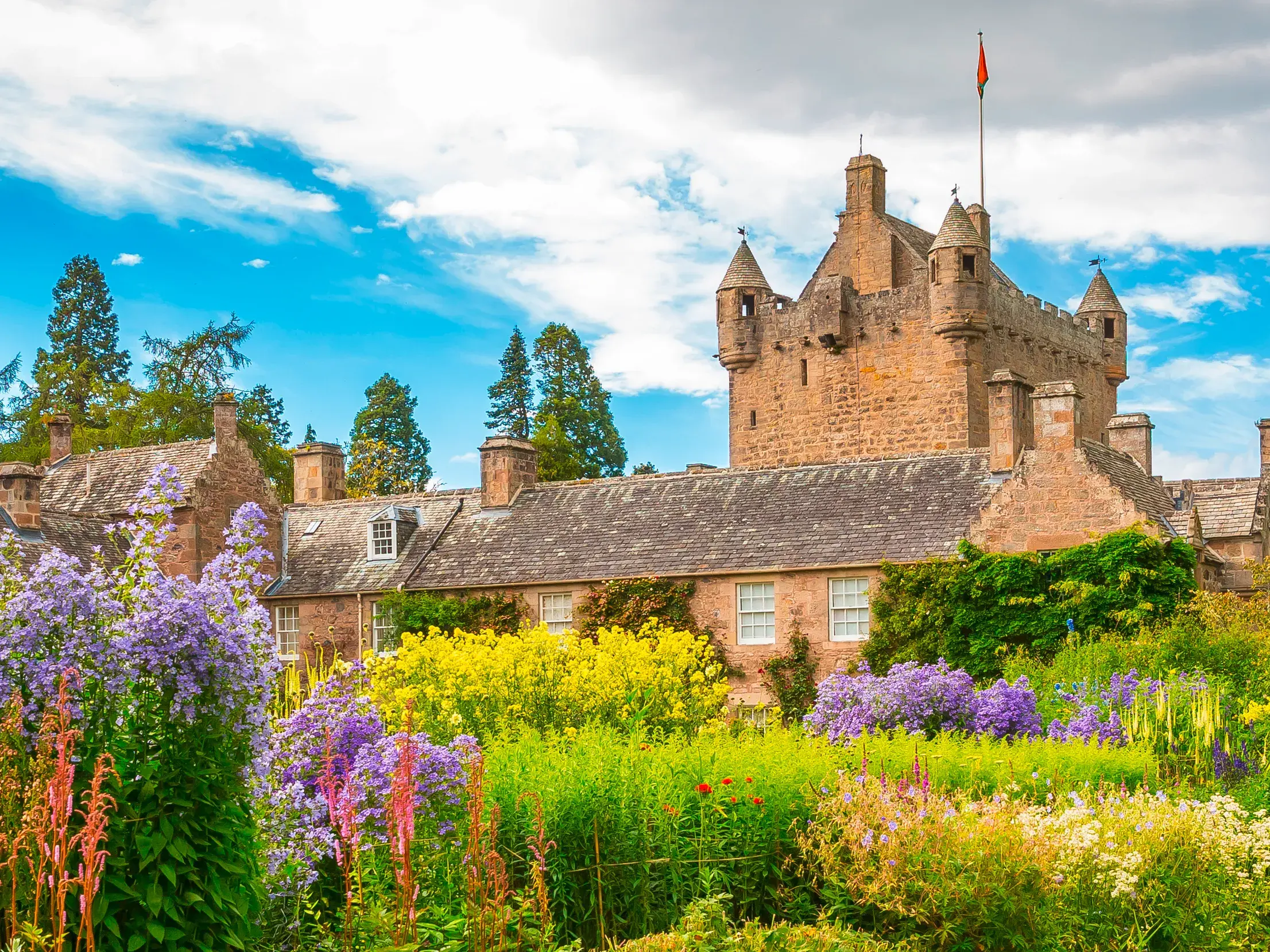 Das historische Zauberschloss Cawdor in Schottland, umgeben von seinen prächtigen, farbenfrohen Gärten unter blauem Himmel.