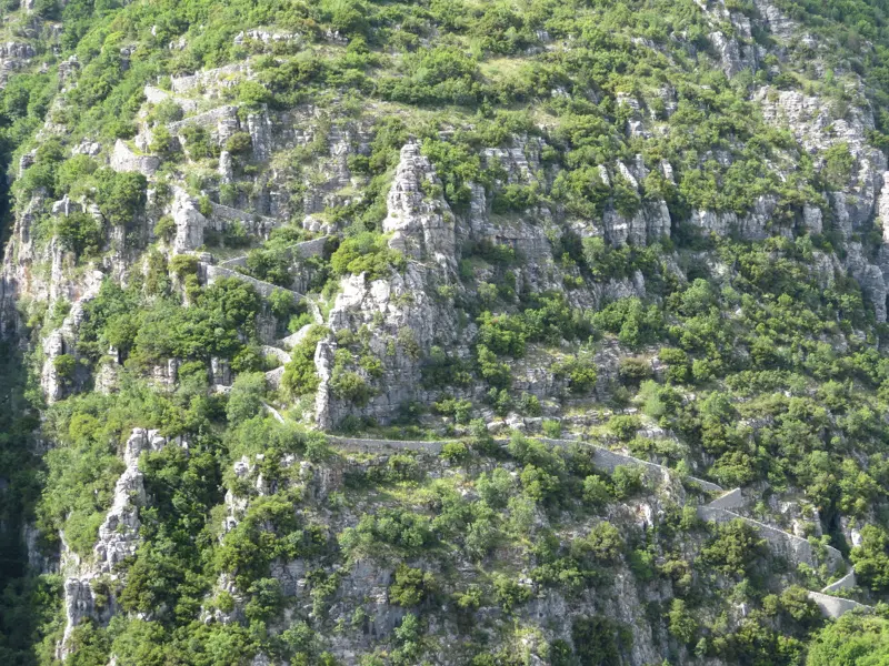 Ein steinerner Serpentinen-Wanderweg, eine historische Skala, windet sich den grünen Felshang in der Vikos-Schlucht hinauf.