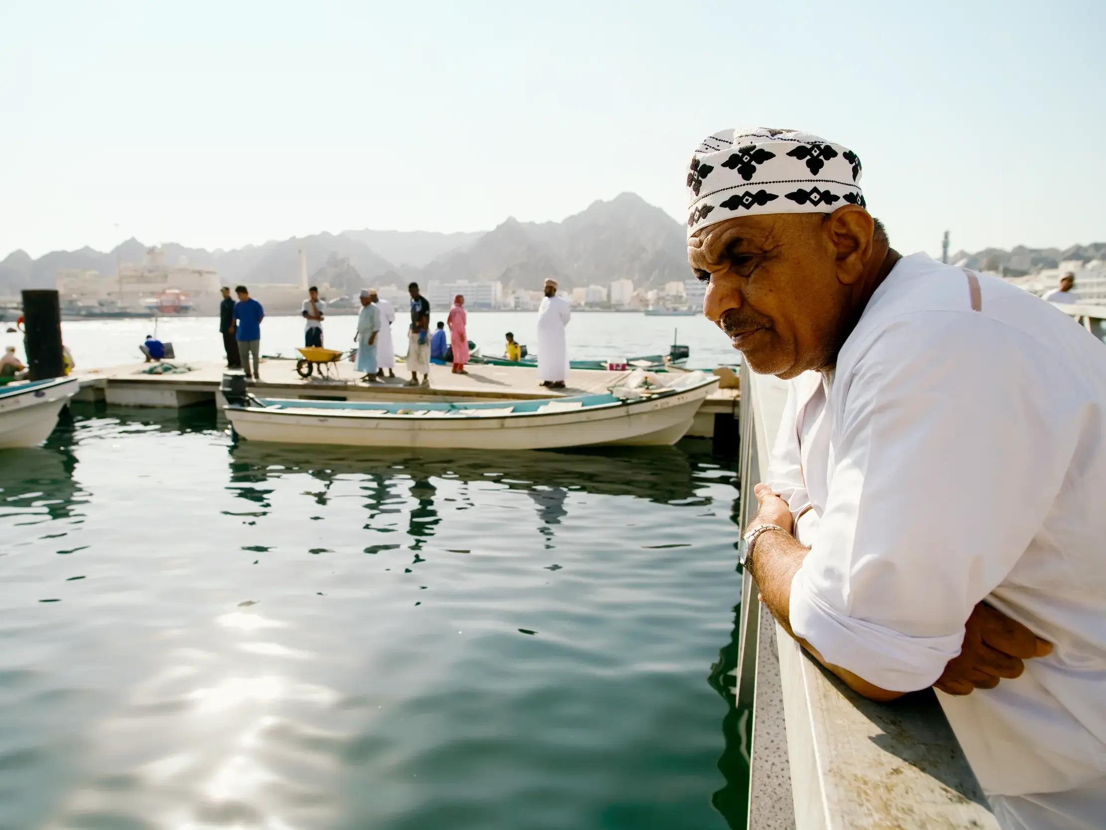 Einheimischer Mann in traditioneller Kleidung blickt nachdenklich über den sonnigen Hafen von Muttrah in Maskat, Oman.