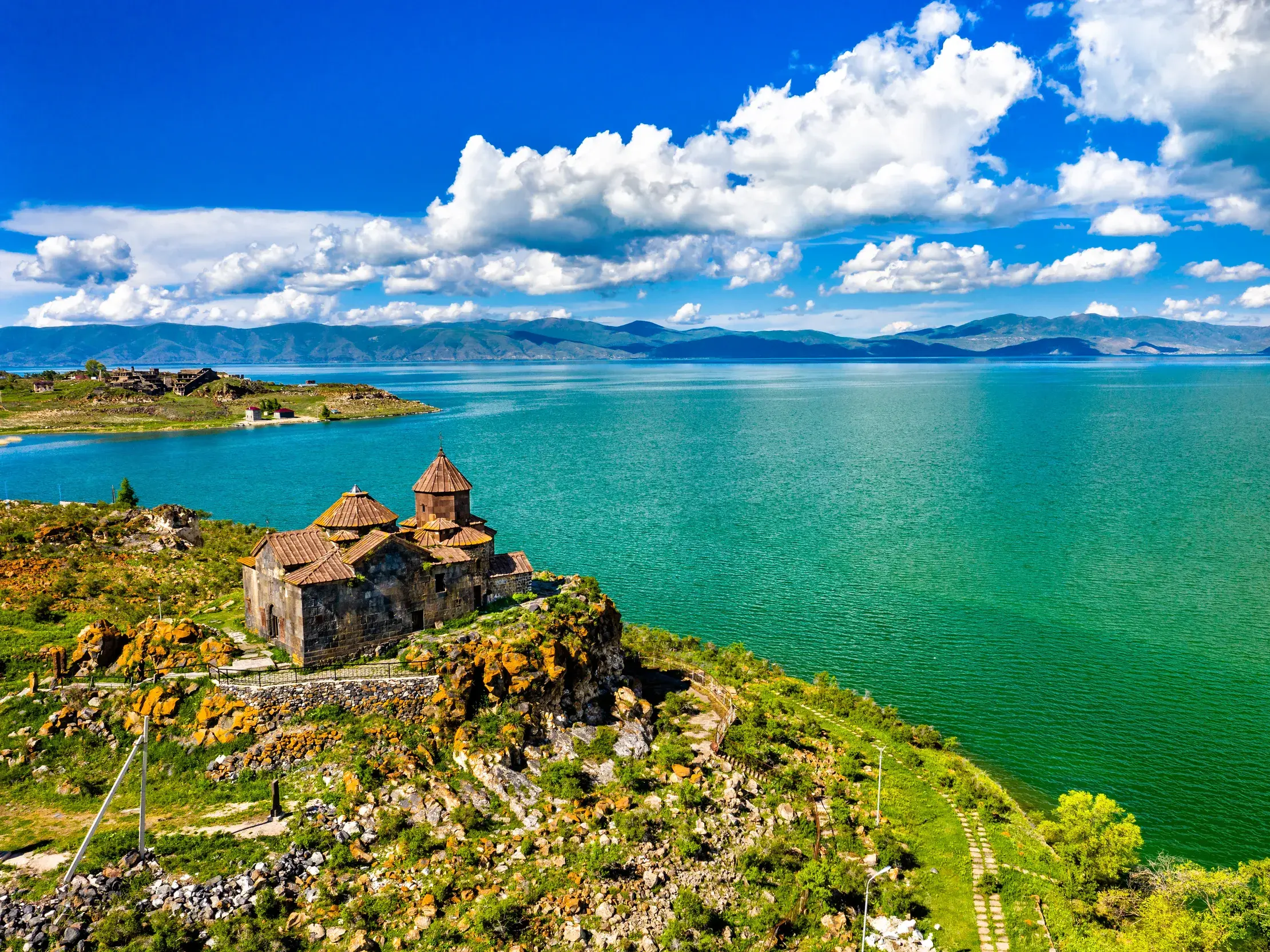 Panoramablick auf das alte Sewankloster am Ufer des leuchtend grünen Sewansees in Armenien mit Bergpanorama im Hintergrund.