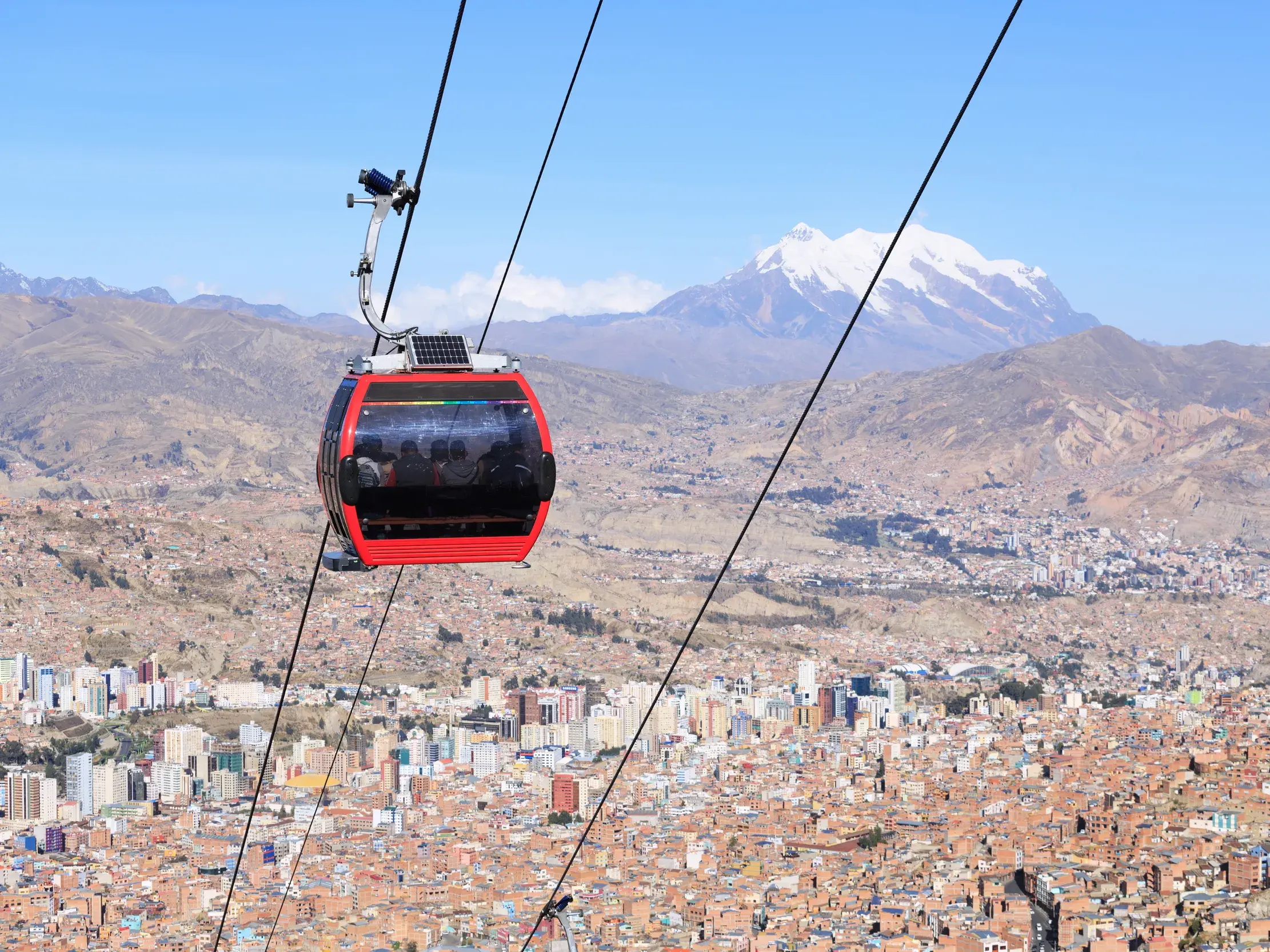 Rote Teleférico-Gondel mit Reisenden schwebt über den Dächern von La Paz vor dem schneebedeckten Berg Illimani in Bolivien.