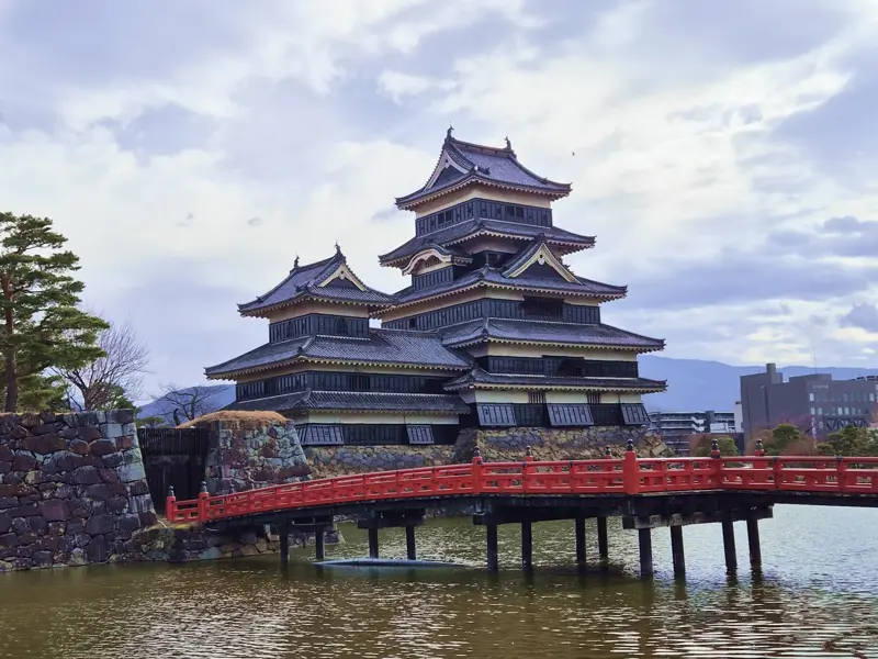 Die imposante Krähenburg Matsumoto in den Japanischen Alpen mit der roten Brücke, die über den Wassergraben führt.