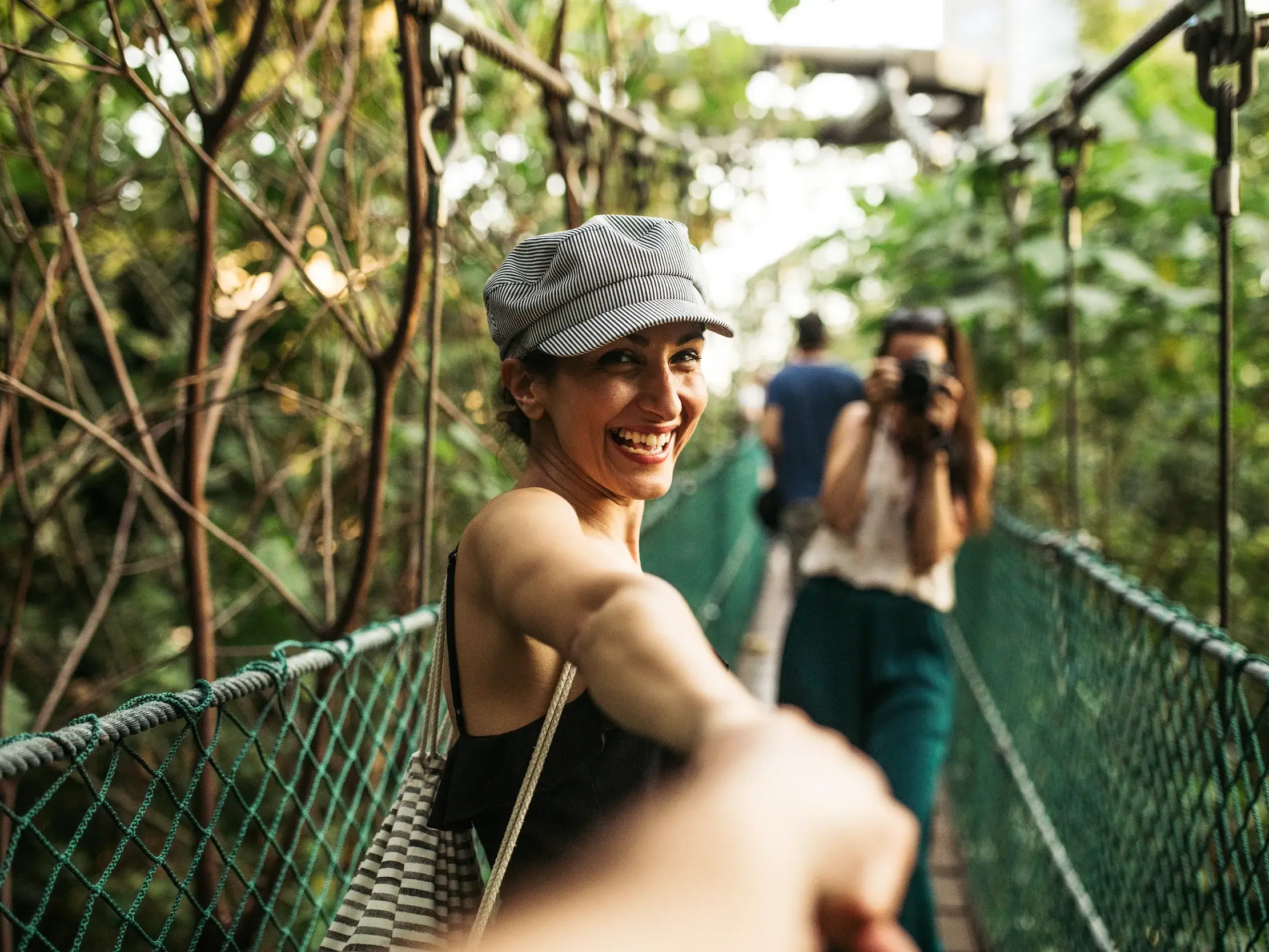 Eine junge Frau führt auf einer Kleingruppenreise in Ecuador eine Person lachend über eine abenteuerliche Hängebrücke im Nebelwald.