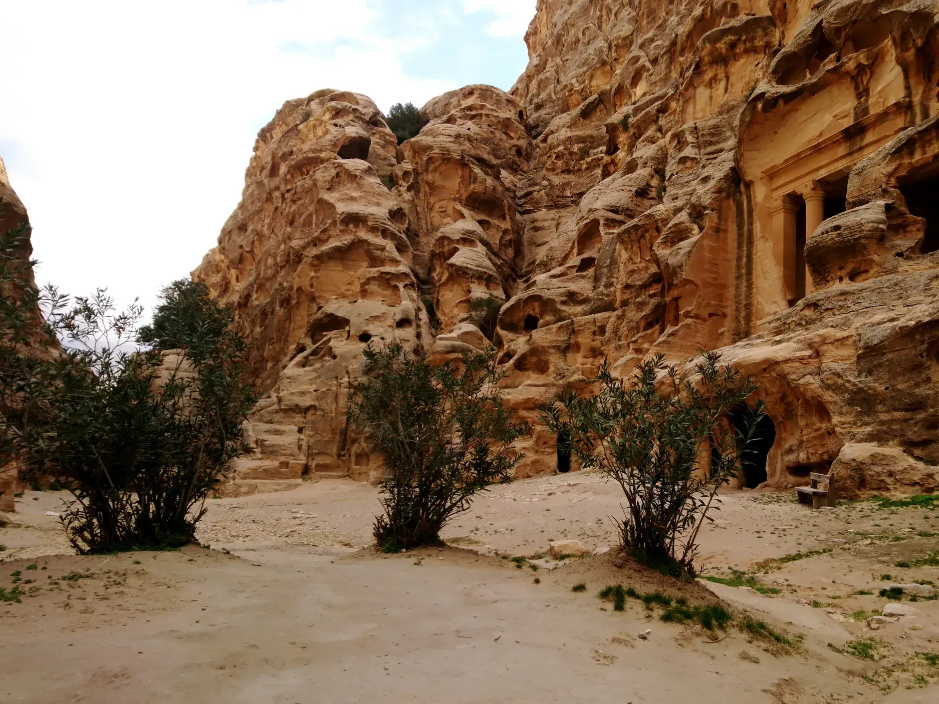 Ein sandiger Wanderweg führt durch die Schlucht Siq al Barid in Jordanien, vorbei an antiken, in den Fels gehauenen Gräbern.