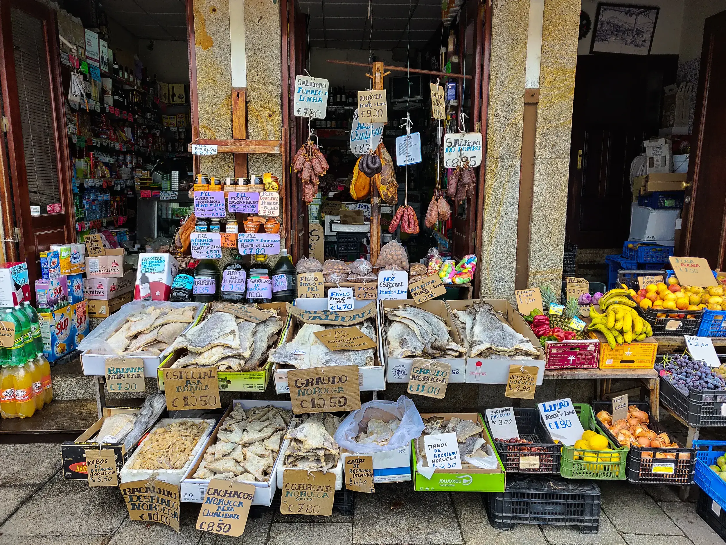 Authentische Auslage eines portugiesischen Delikatessengeschäfts mit Stockfisch (Bacalhau), Wurstwaren und frischem Obst.