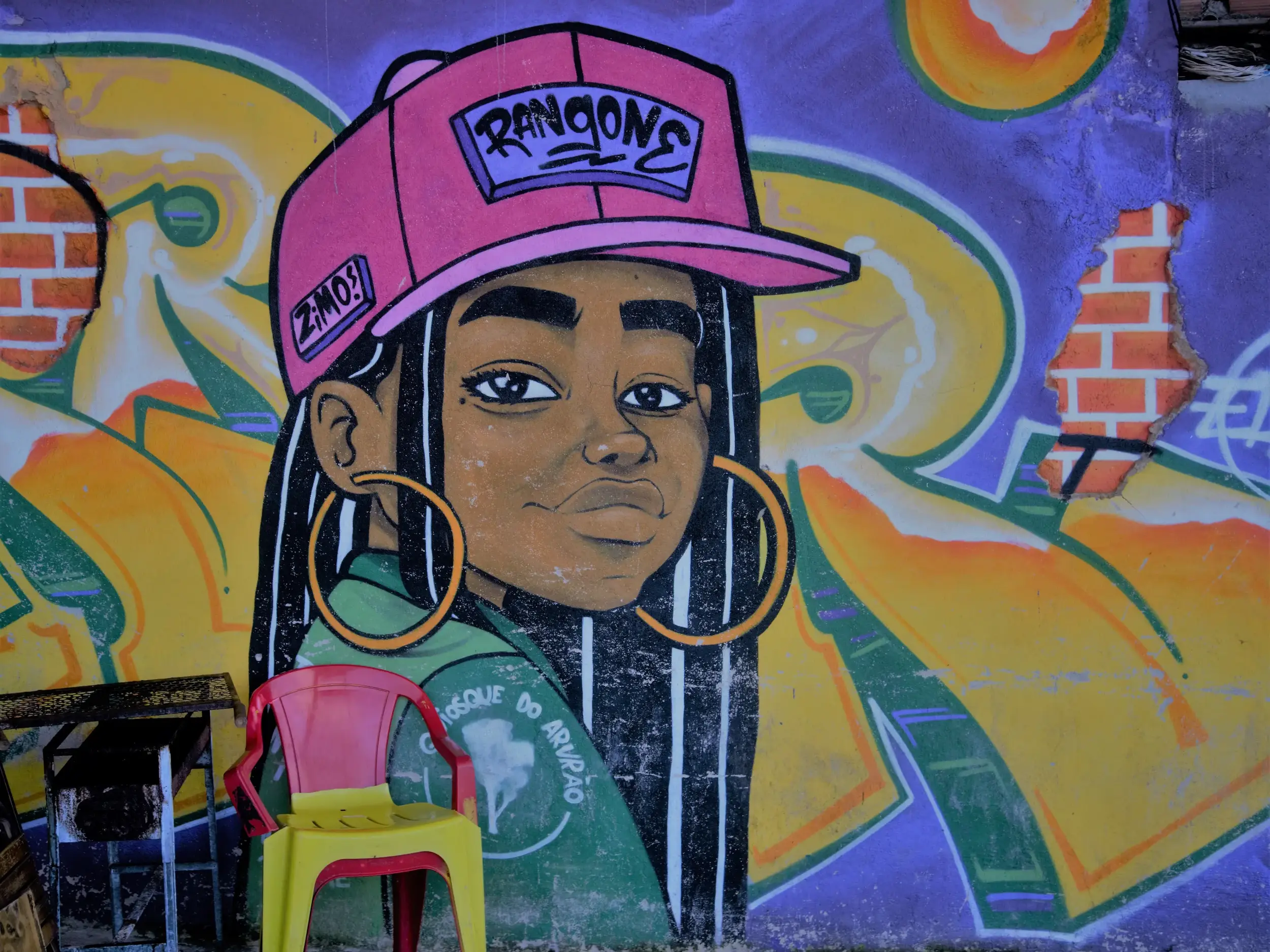 Farbenfrohes Graffiti einer Frau mit pinker Kappe an einer Hauswand in der Favela Morro da Babilônia in Rio de Janeiro.