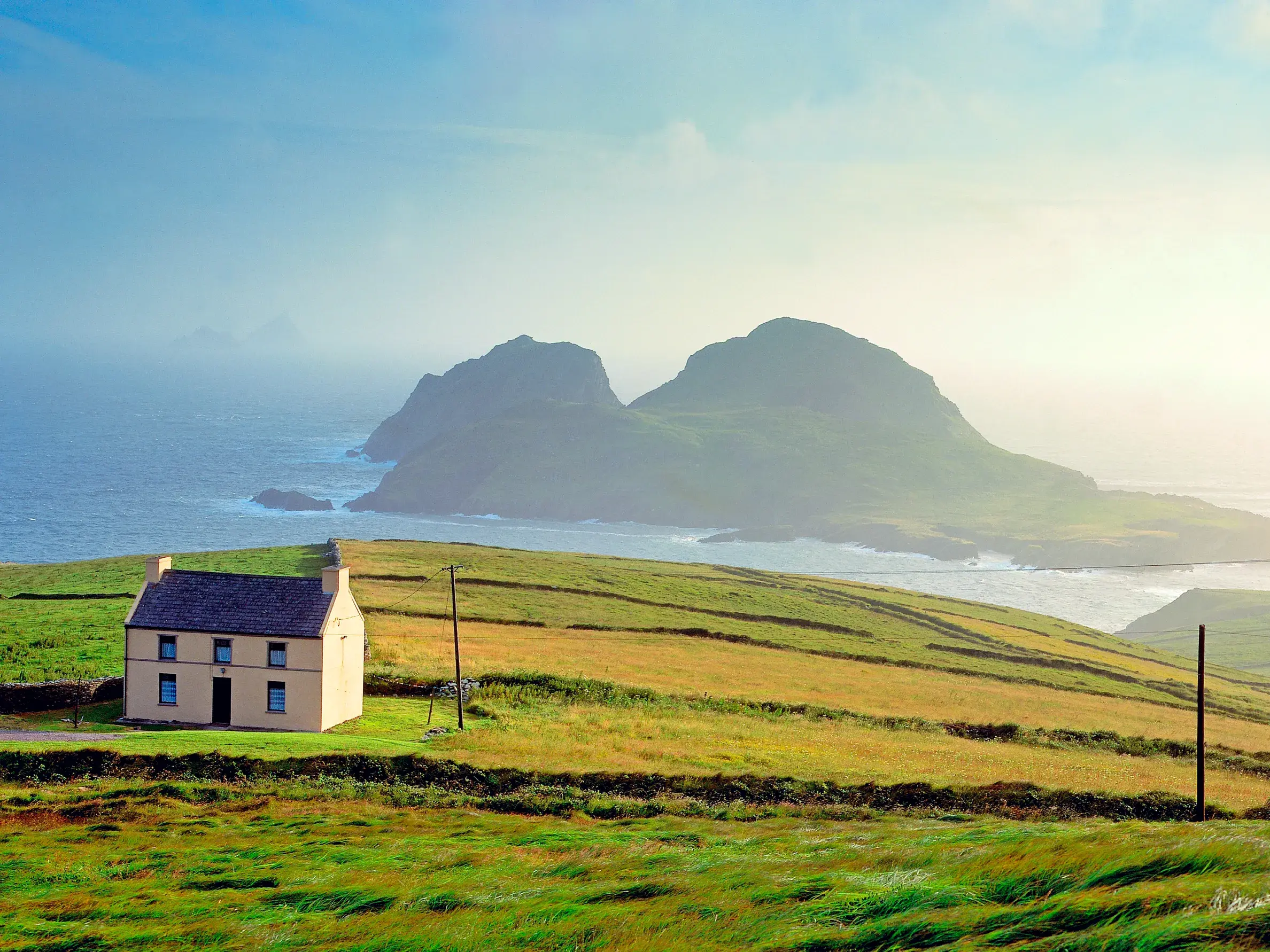 Idyllisches Cottage in den grünen Hügeln der Halbinsel Dingle mit Blick auf den Atlantischen Ozean und Inseln.