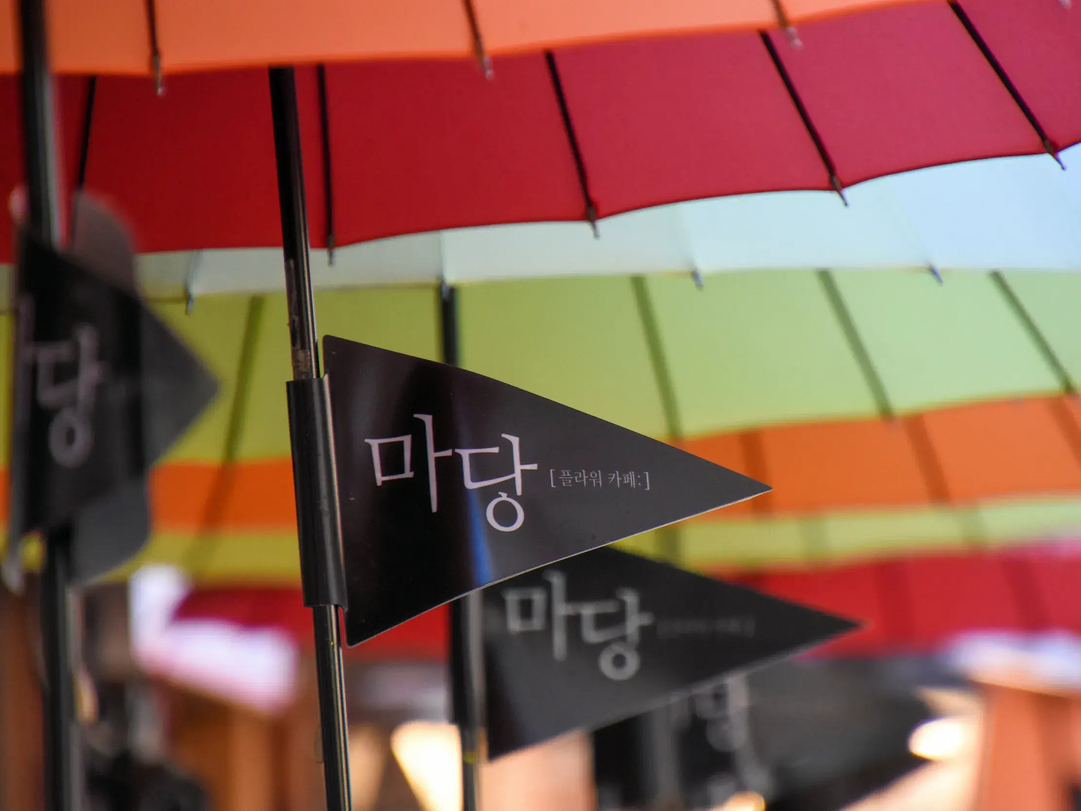 Schwarze Wimpel mit koreanischer Schrift unter bunten Regenschirmen auf einer Kleingruppenreise durch Südkorea.