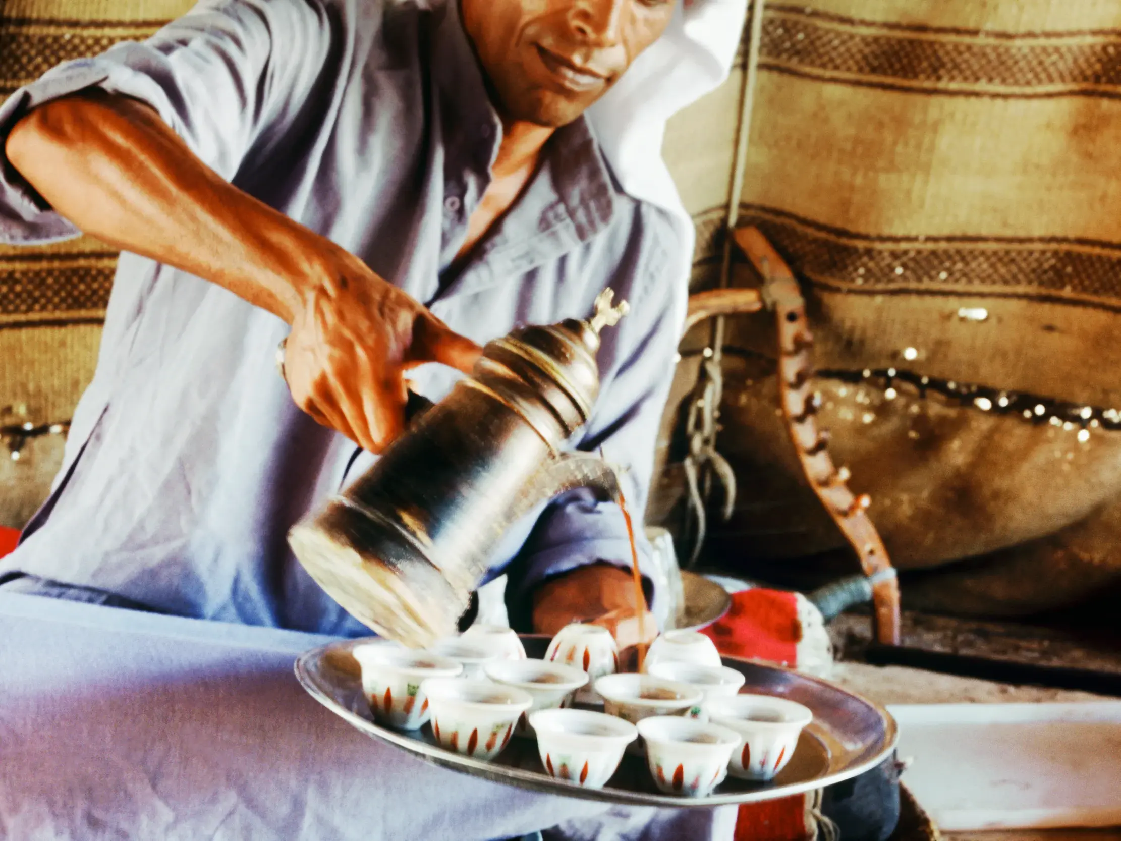 Ein Beduine in traditioneller Kleidung gießt als Geste der Gastfreundschaft in Israel Kaffee in kleine Tassen.
