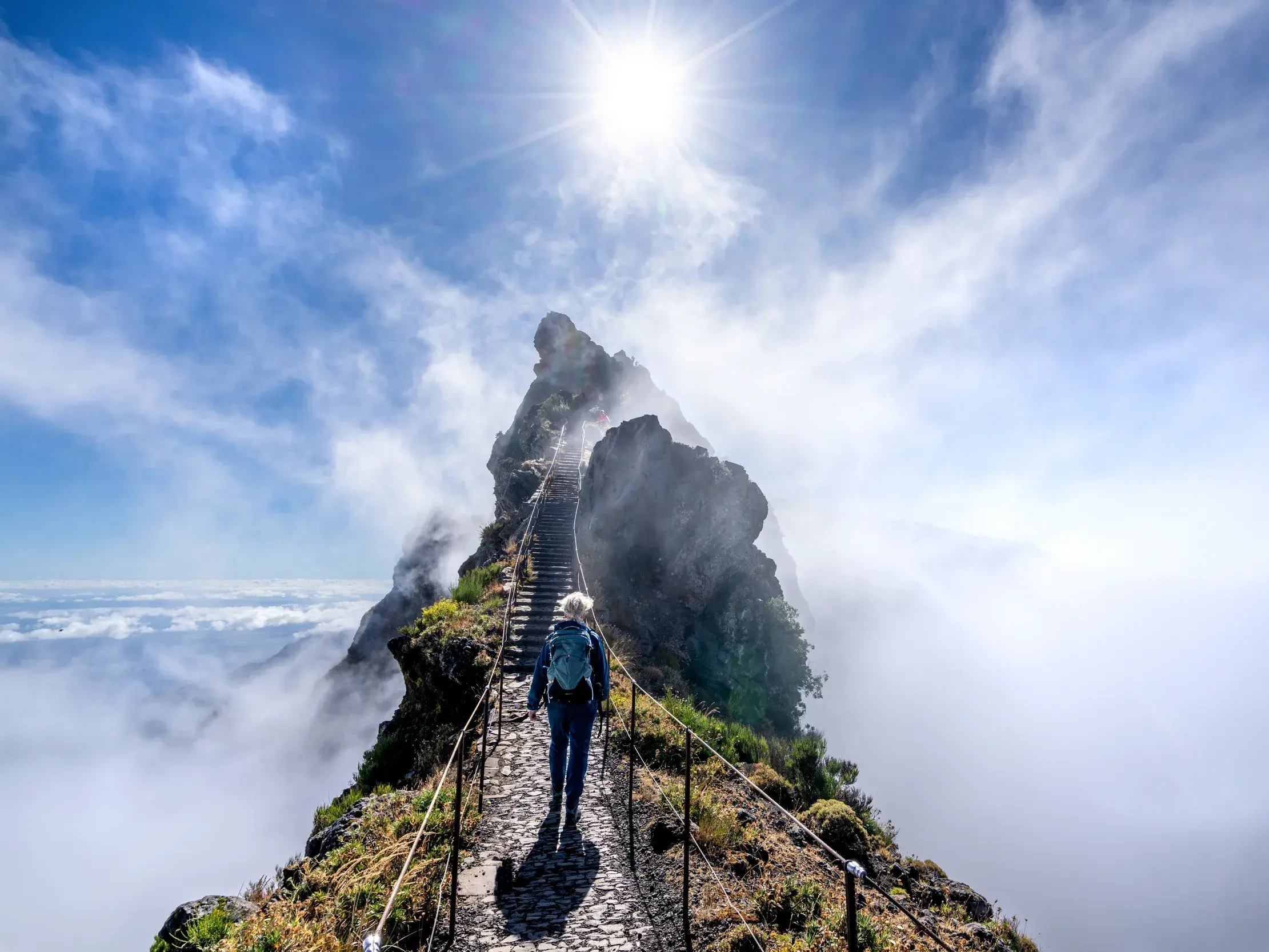 Eine Person wandert auf dem gesicherten Gebirgspfad zwischen Pico do Arieiro und Pico Ruivo über den Wolken Madeiras.