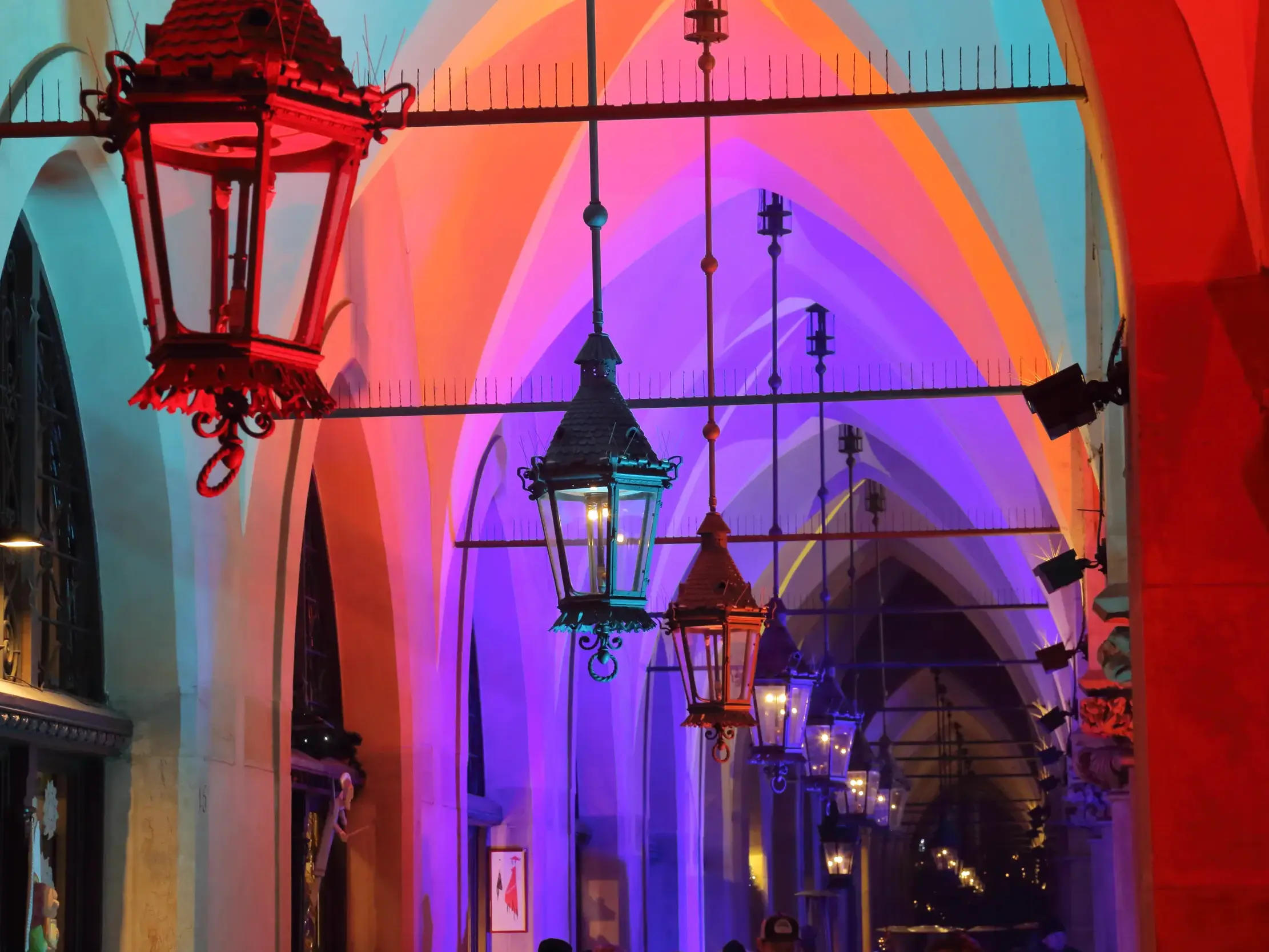 Historische Laternen in den abendlich bunt beleuchteten Arkaden der Tuchhallen in der Altstadt von Krakau.