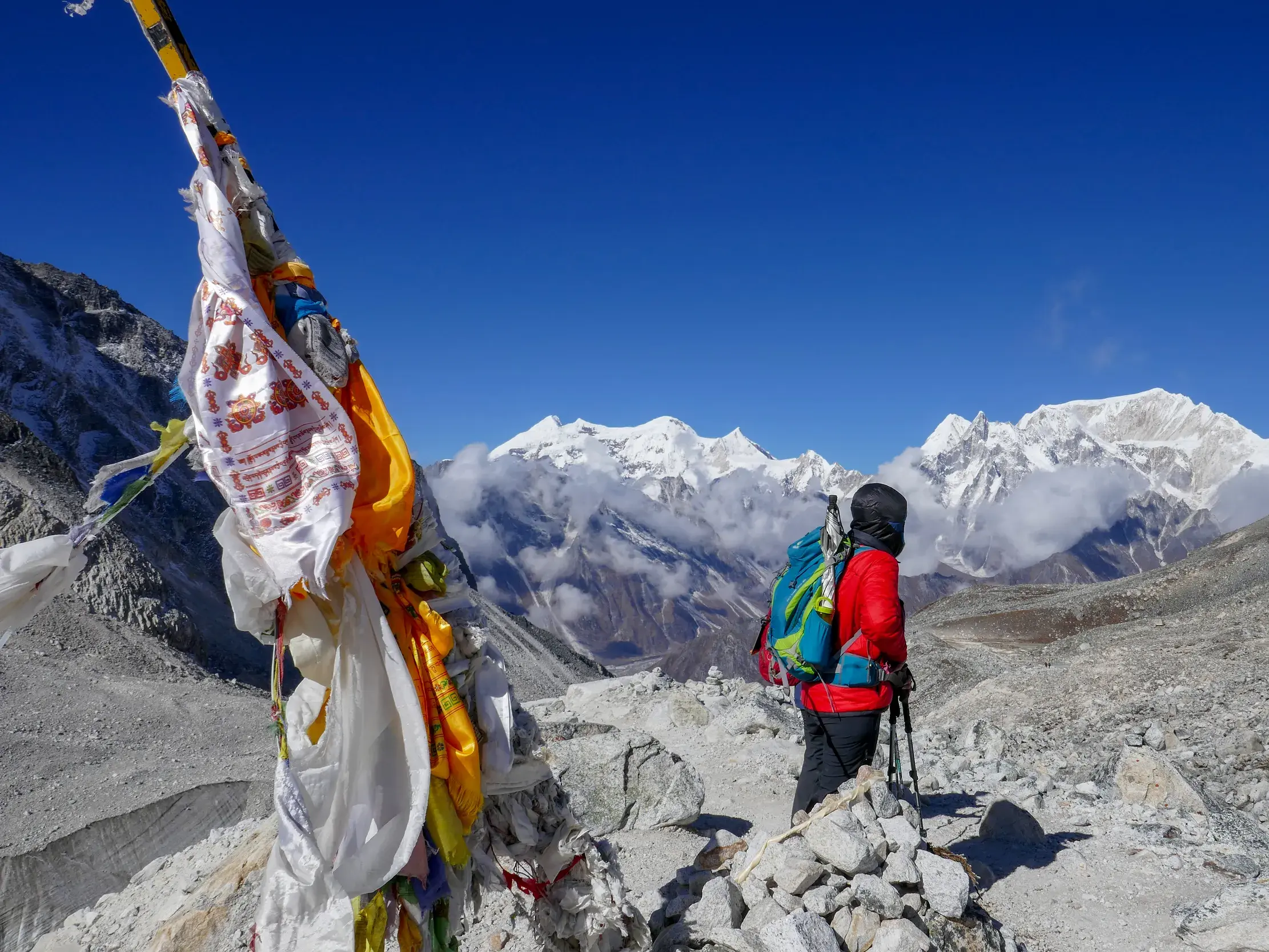 Ein Wanderer mit Rucksack pausiert neben Gebetsfahnen am Larkya-Pass und blickt auf das Panorama des Manaslu Himal in Nepal.