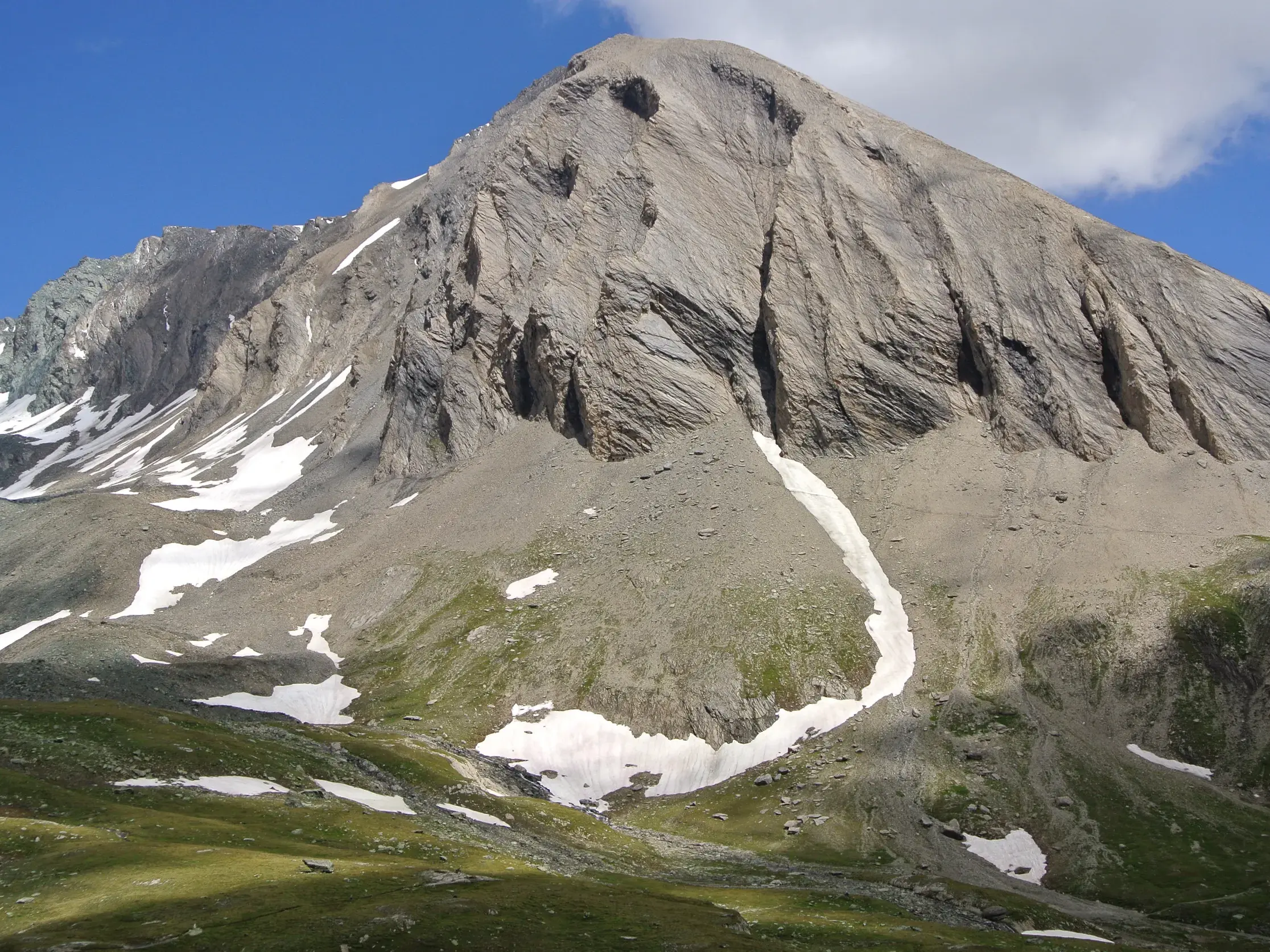 Ein karger Felsgipfel mit Schneefeldern und grünen Almwiesen im Nationalpark Hohe Tauern auf der Glocknerrunde.