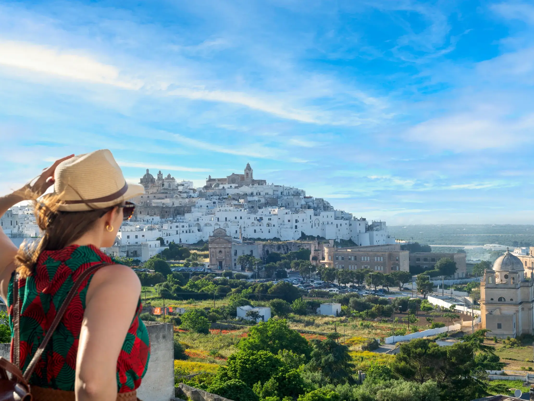 Eine Reisende mit Hut genießt den Panoramablick auf die auf einem Hügel erbaute weiße Stadt Ostuni in Apulien.