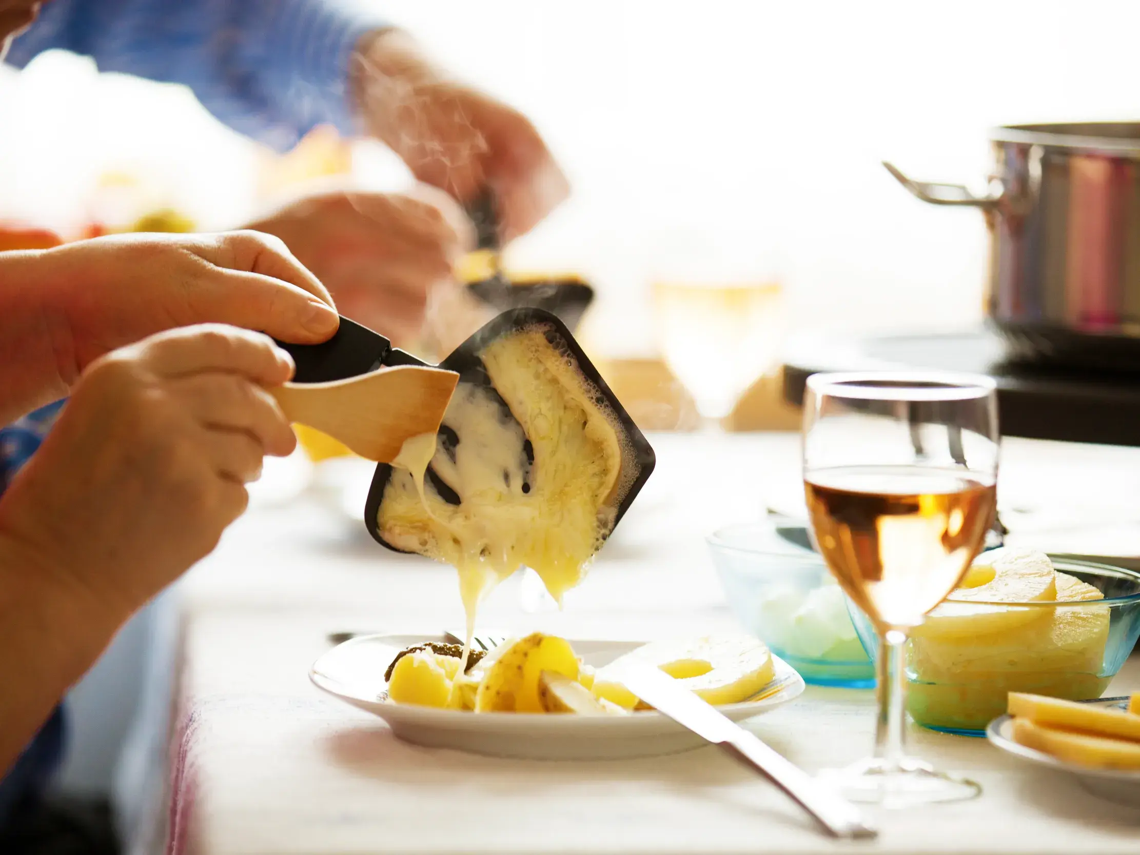 Eine Person streicht geschmolzenen Raclette-Käse von einem Pfännchen auf Kartoffeln bei einem Abendessen in der Schweiz.
