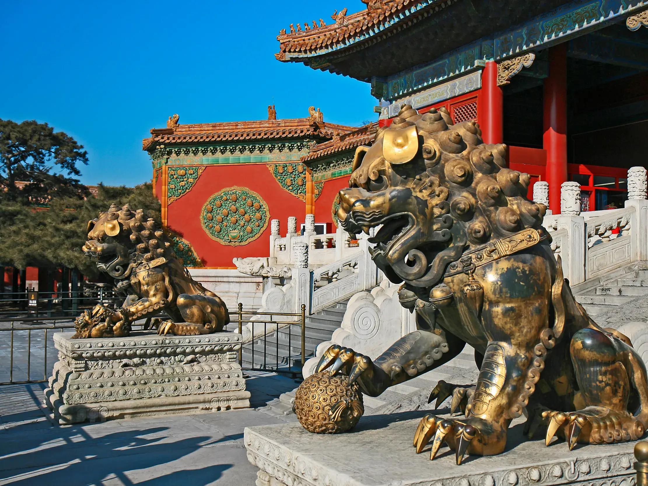 Zwei imposante, goldene Wächterlöwen bewachen den Eingang zum Kaiserpalast in Peking bei strahlend blauem Himmel.