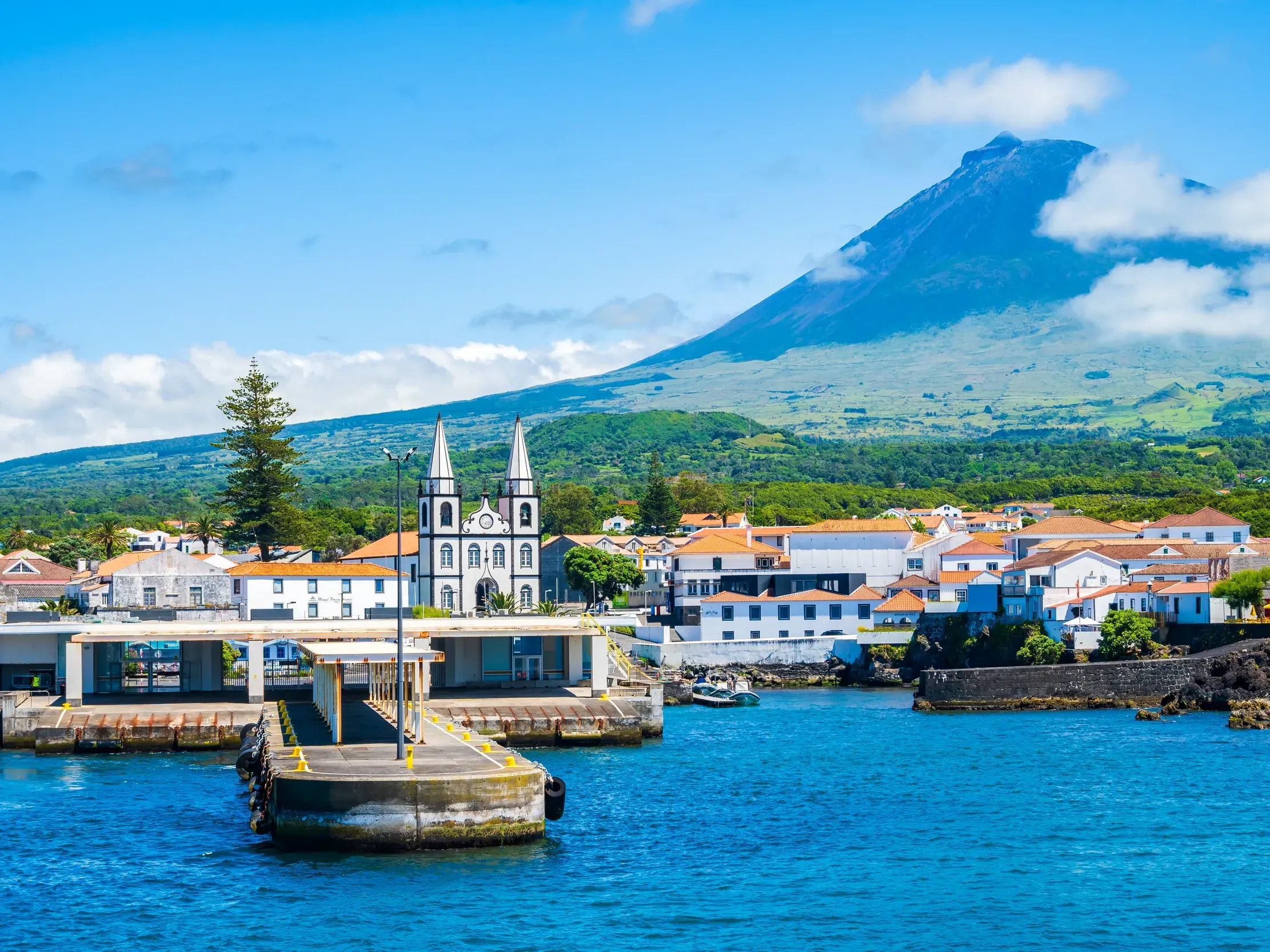 Hafeneinfahrt von Madalena auf der Azoren-Insel Pico mit der Kirche und dem majestätischen Vulkan Pico im Hintergrund.