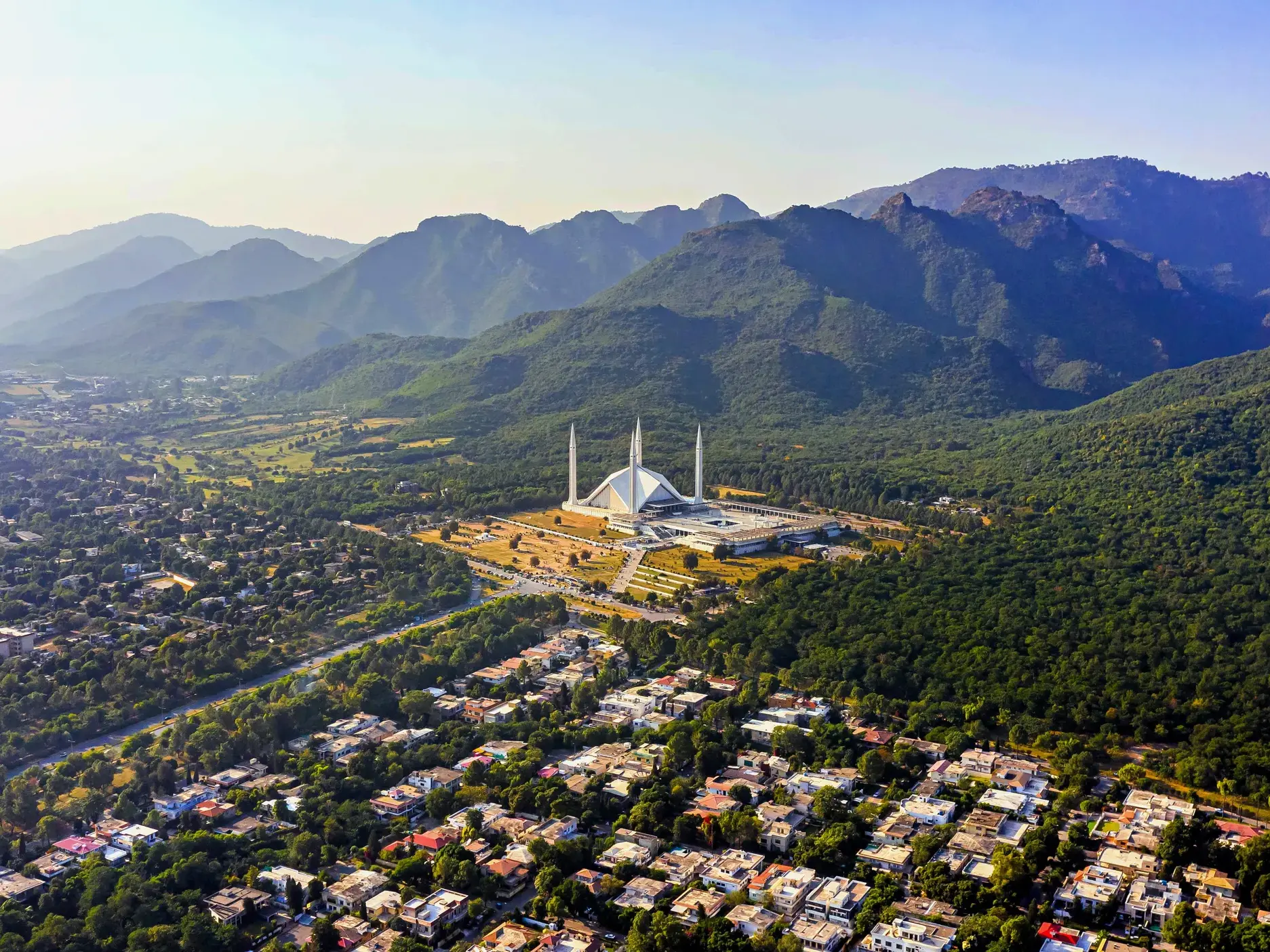 Luftaufnahme der modernen Faisal-Moschee in Islamabad vor der grünen Bergkulisse der Margalla-Hügel am Beginn der Trekkingreise.