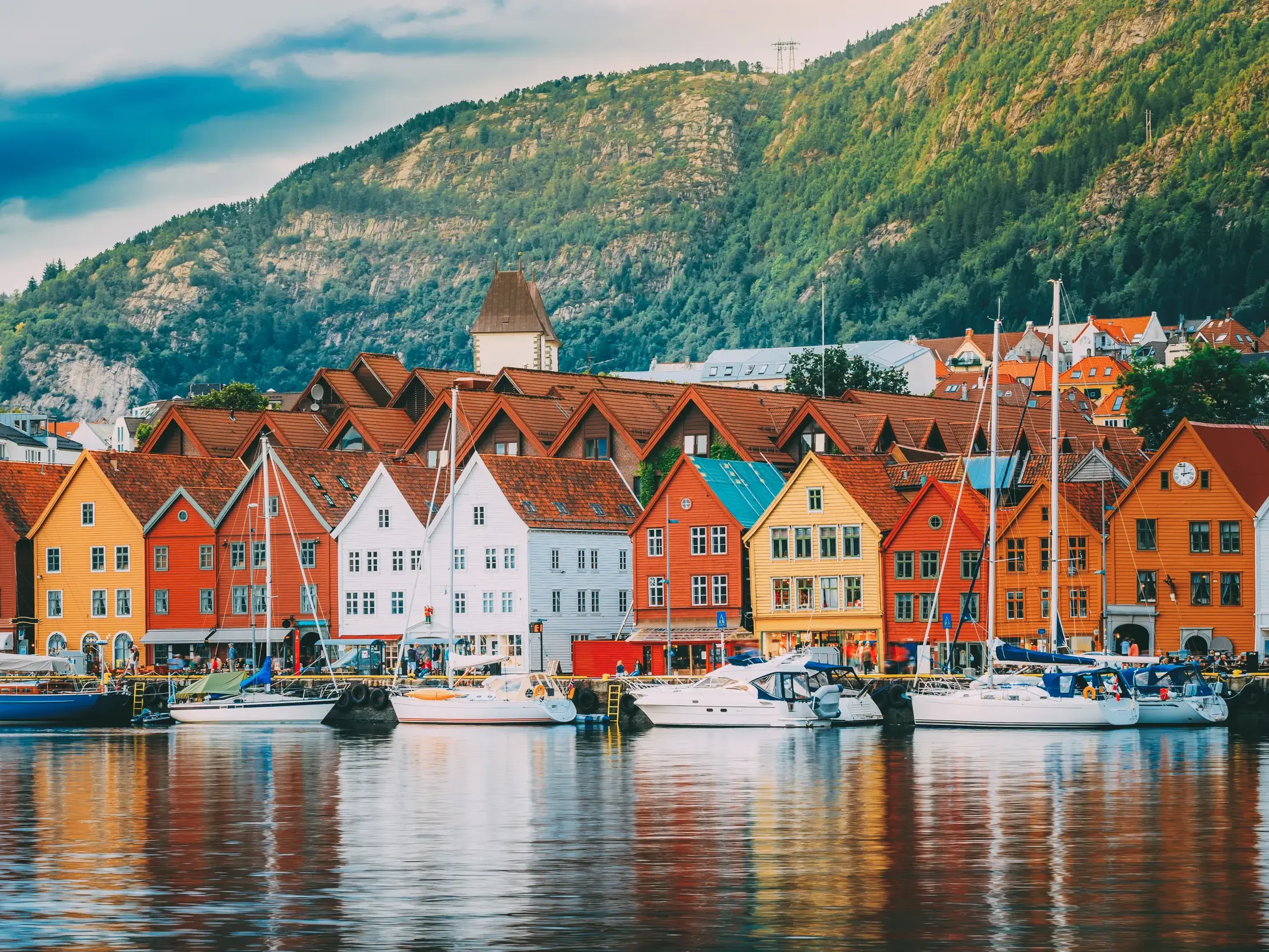 Die farbenfrohen Holzhäuser des Hanseviertels Bryggen, UNESCO-Welterbe in Bergen, säumen den Hafen vor dem Berg Flöyen.