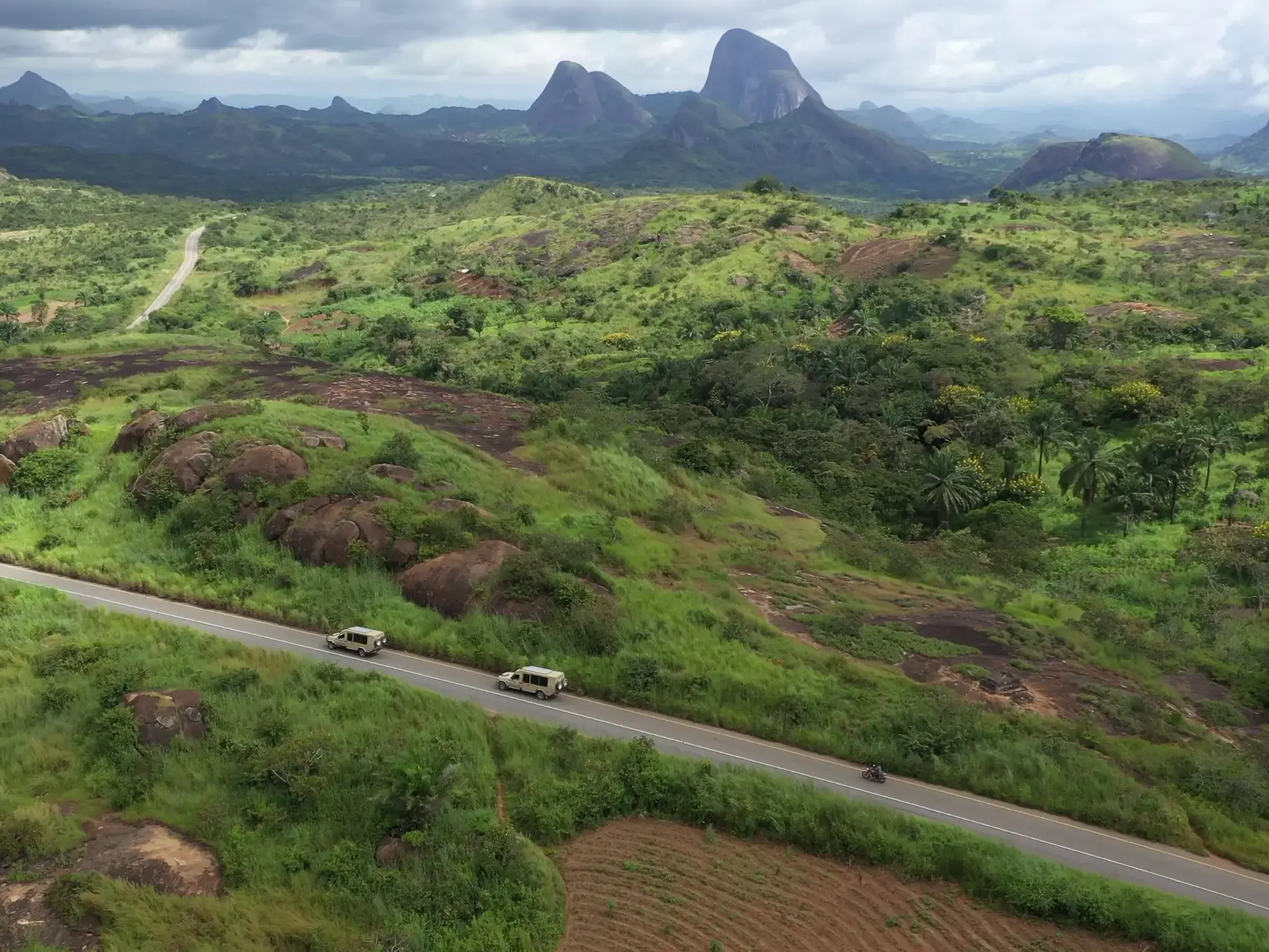 Zwei Reisefahrzeuge auf dem Weg durch die grüne Savannen-Landschaft zu den markanten Schwarzen Felsen von Pungo Andongo in Angola.