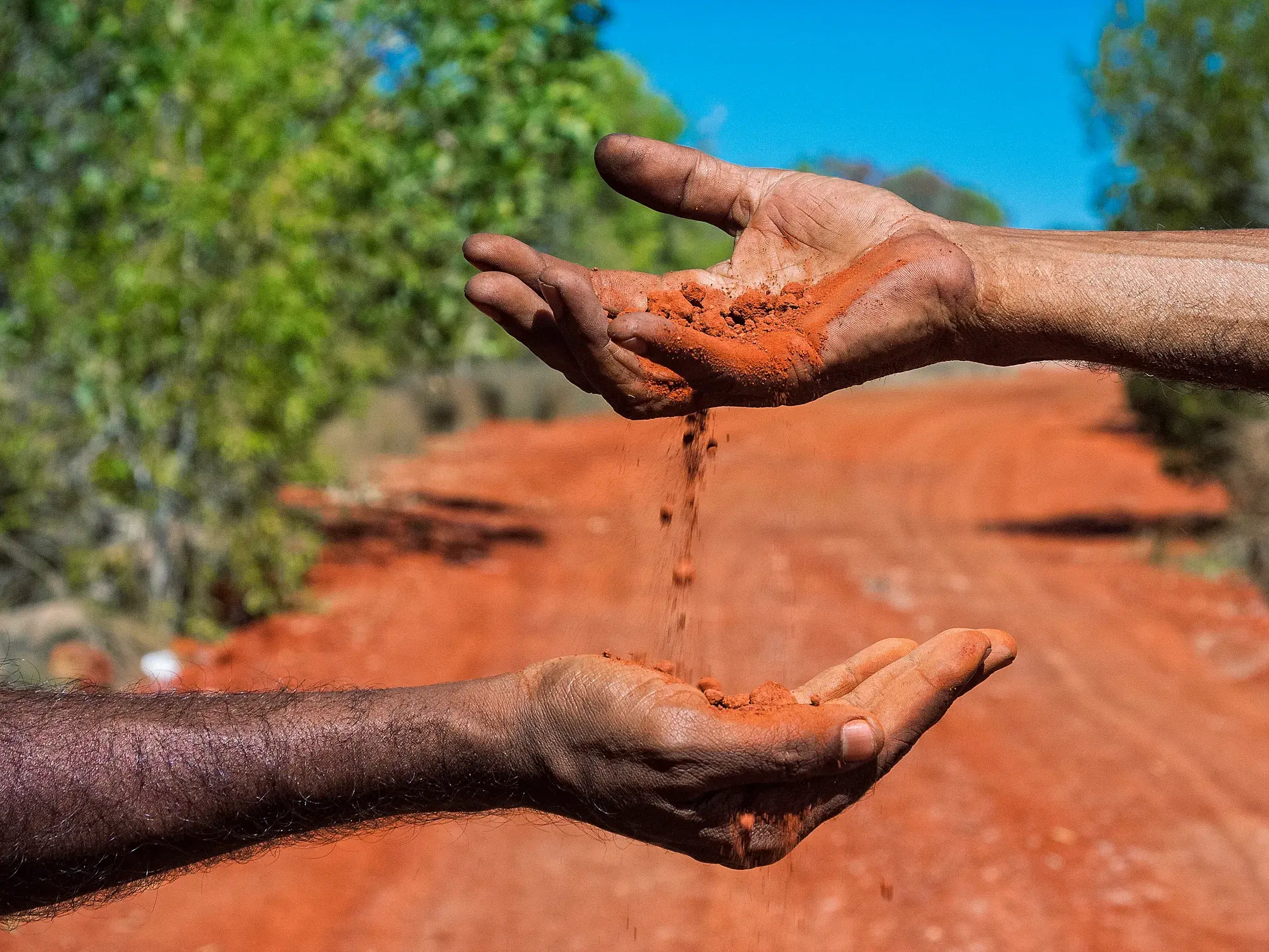 Rote Erde des Outbacks rieselt durch die Hände zweier Menschen als Symbol für die Kultur der Aboriginals in Australien.