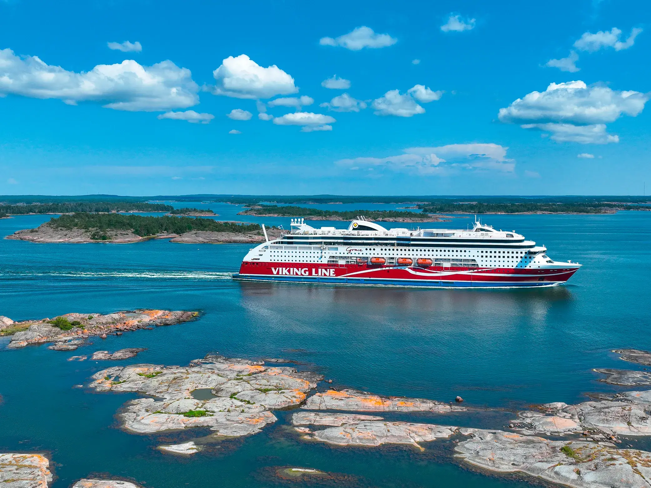 Eine rot-weiße Fähre der Viking Line navigiert bei Sonnenschein durch die felsige Inselwelt des Schärengartens vor Stockholm.