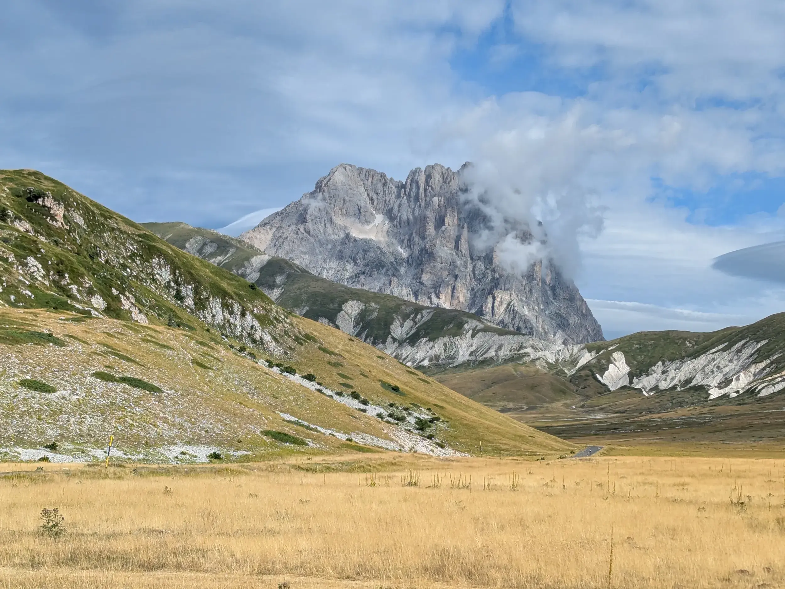 Goldene Wiesen auf der Hochebene Campo Imperatore mit Blick auf den felsigen, wolkenverhangenen Gipfel des Gran Sasso im Apennin.