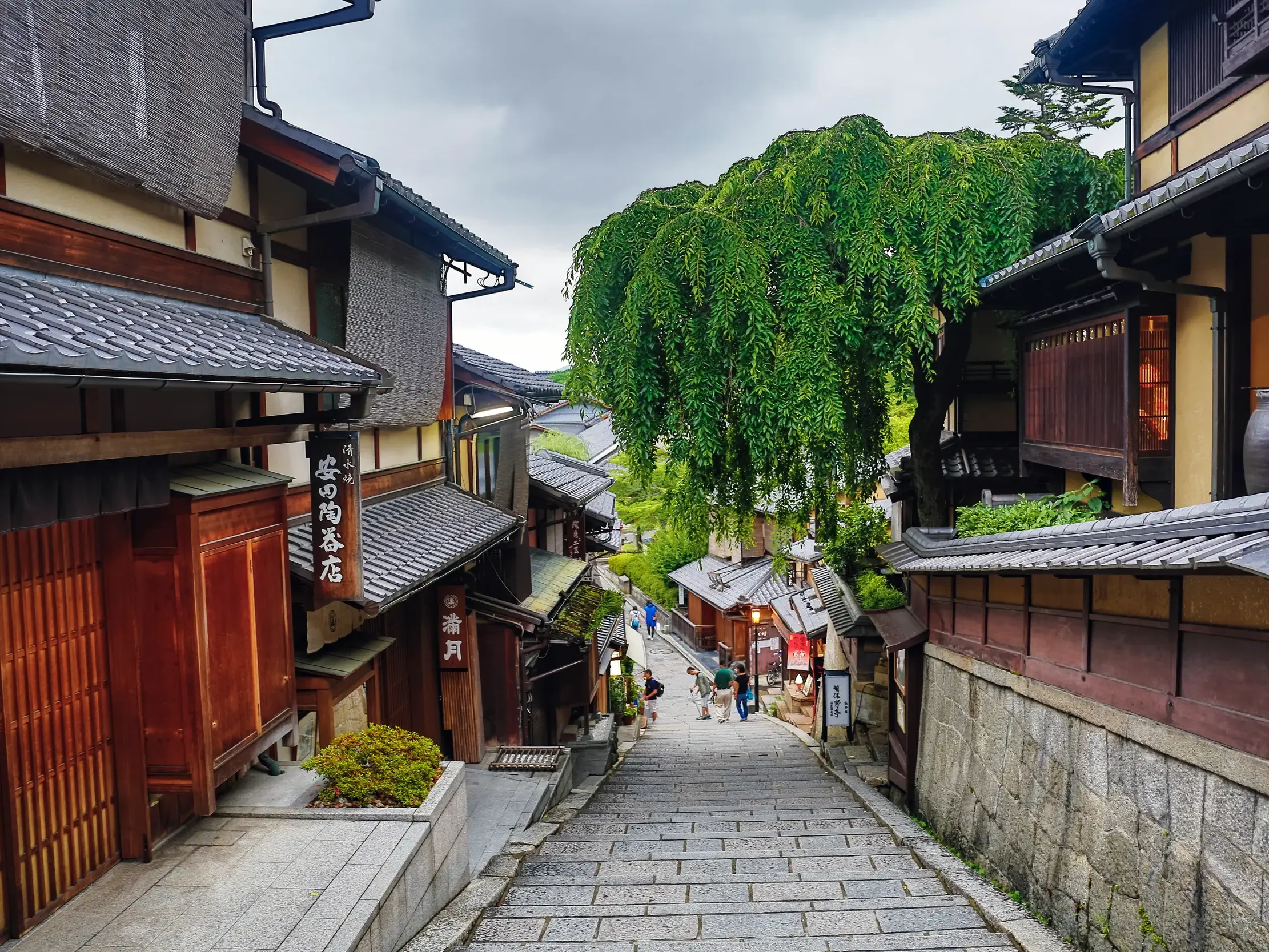 Eine kleine Gruppe junger Leute spaziert eine Steintreppe in einer historischen Gasse des Higashiyama-Viertels in Kyoto hinab.