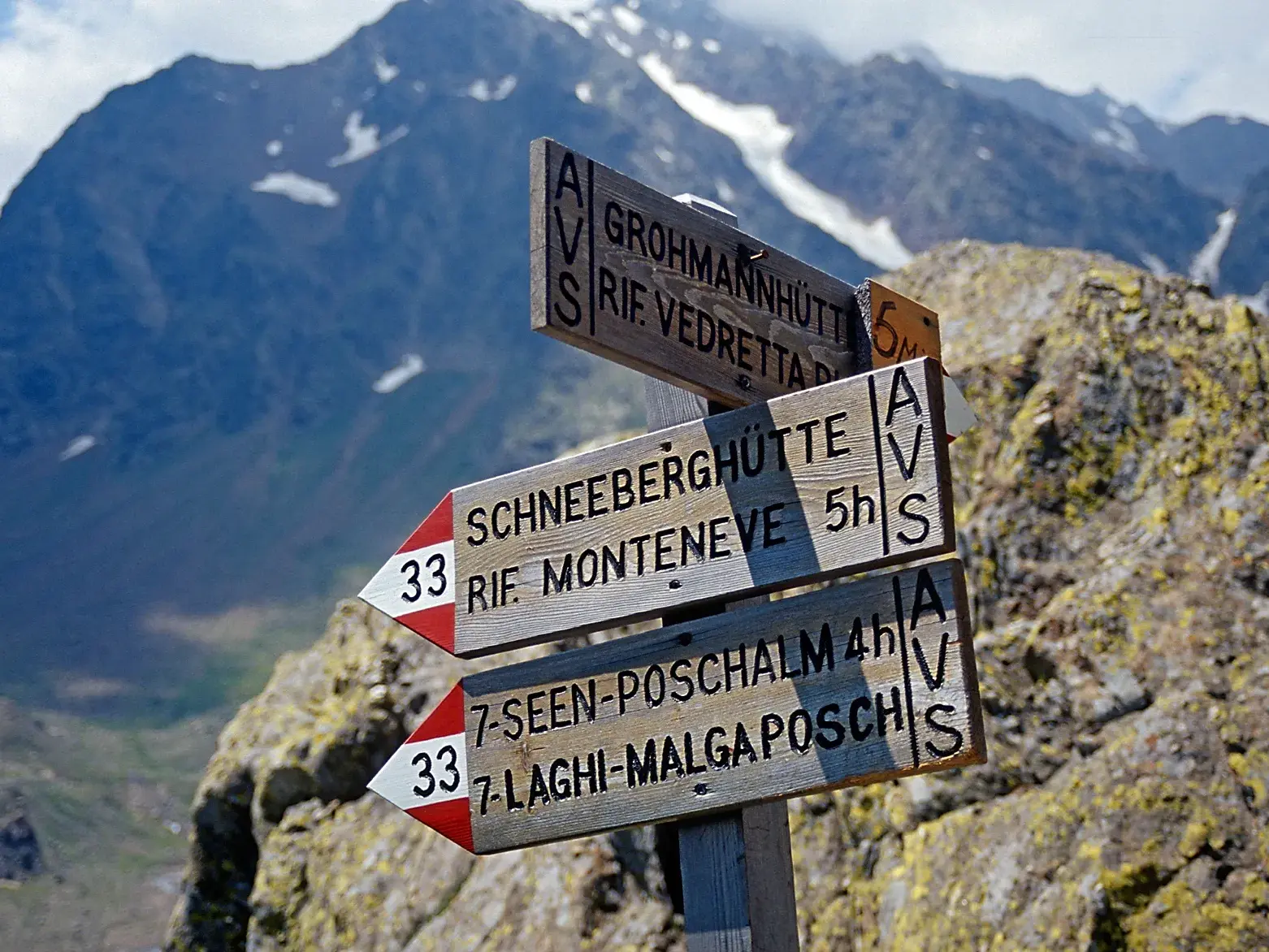 Ein hölzerner Wanderwegweiser in den Stubaier Alpen zeigt die Gehzeiten zur Schneeberghütte, Poschalm und Grohmannhütte.