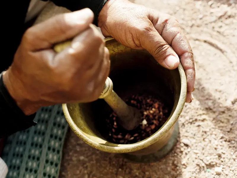 Nahaufnahme von Händen eines Beduinen, die in einem traditionellen Messingmörser aromatische Kaffeebohnen zerstoßen.