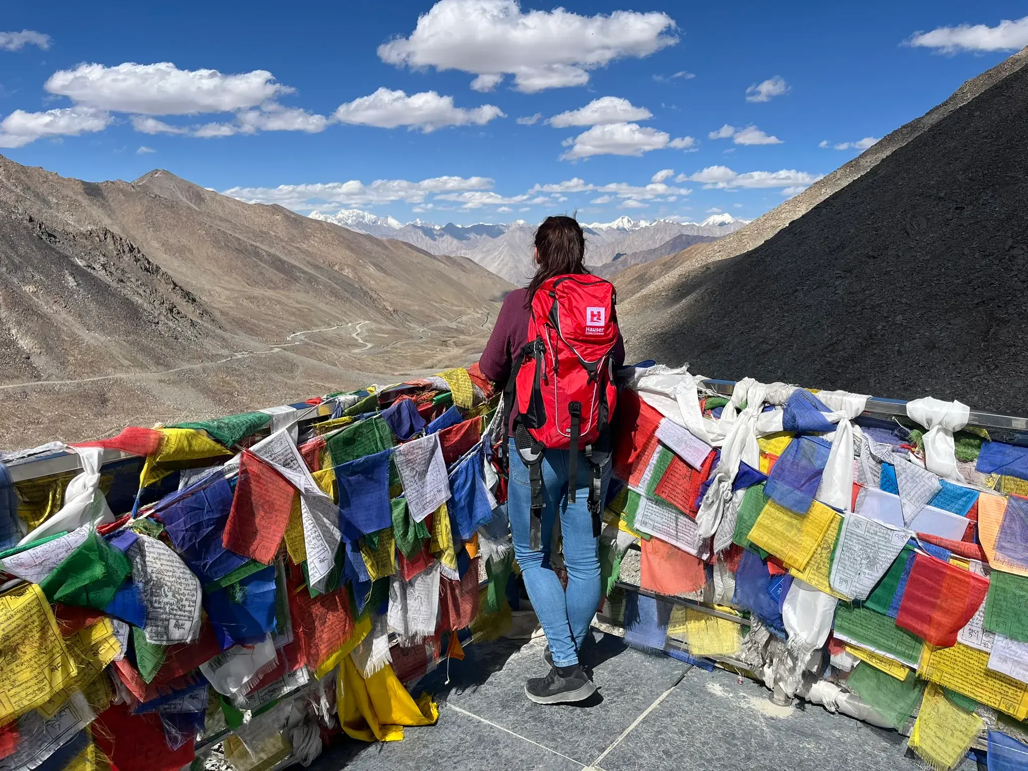 Wanderin  genießt auf dem Khardung La  in Ladakh den Ausblick über bunte Gebetsfahnen auf den Himalaya.