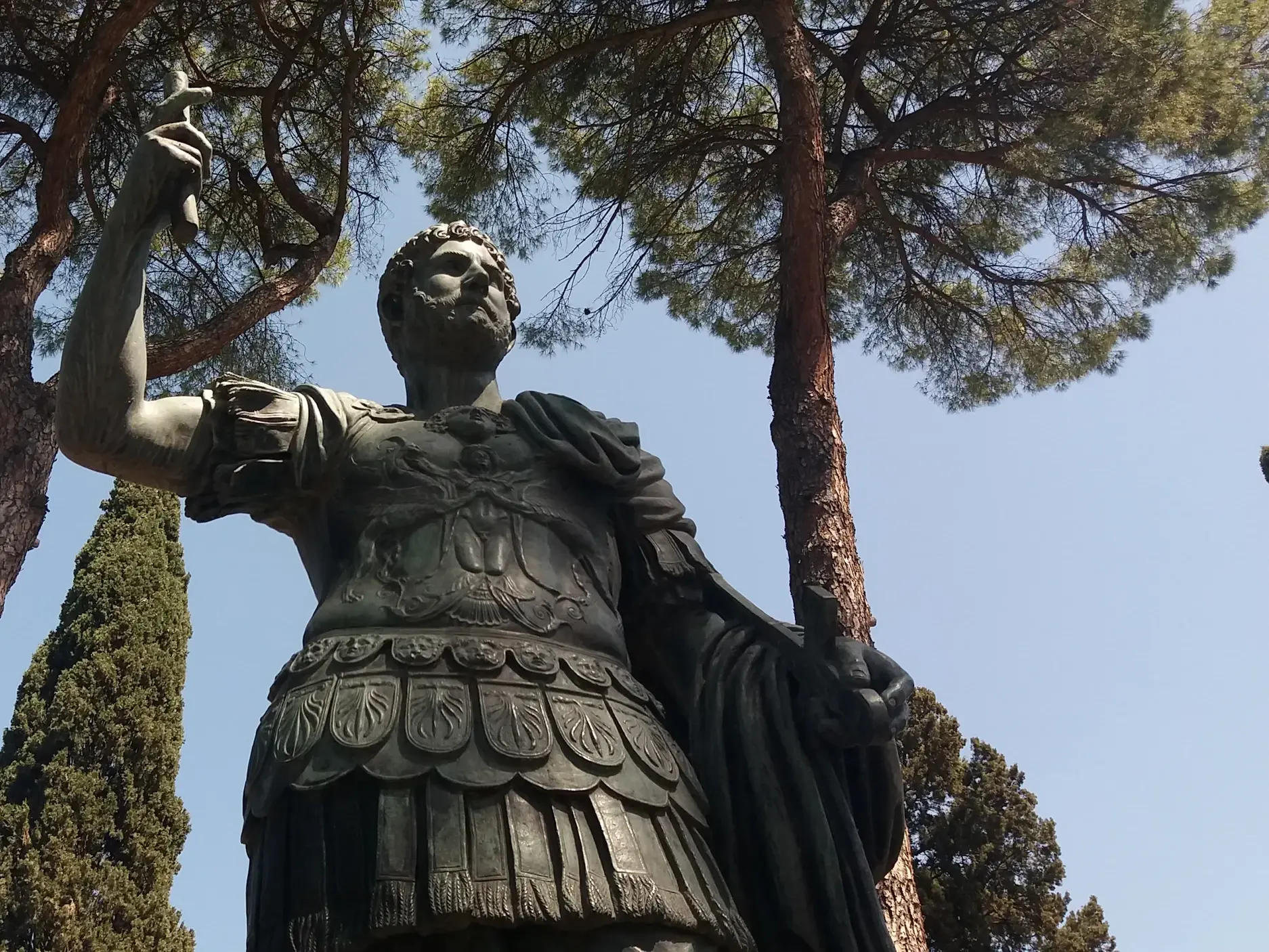 Majestätische Statue eines römischen Imperators in Rüstung, umgeben von Pinienbäumen bei einer Wanderreise in Rom.