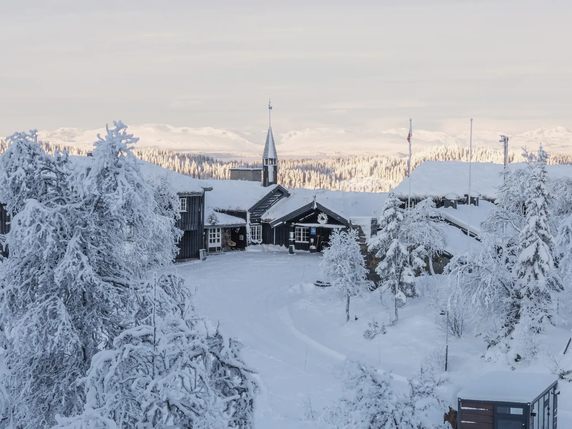 Luftaufnahme der verschneiten Danebu Kongsgaard in Aurdal vor der weiten, winterlichen Bergkulisse von Valdres in Norwegen.