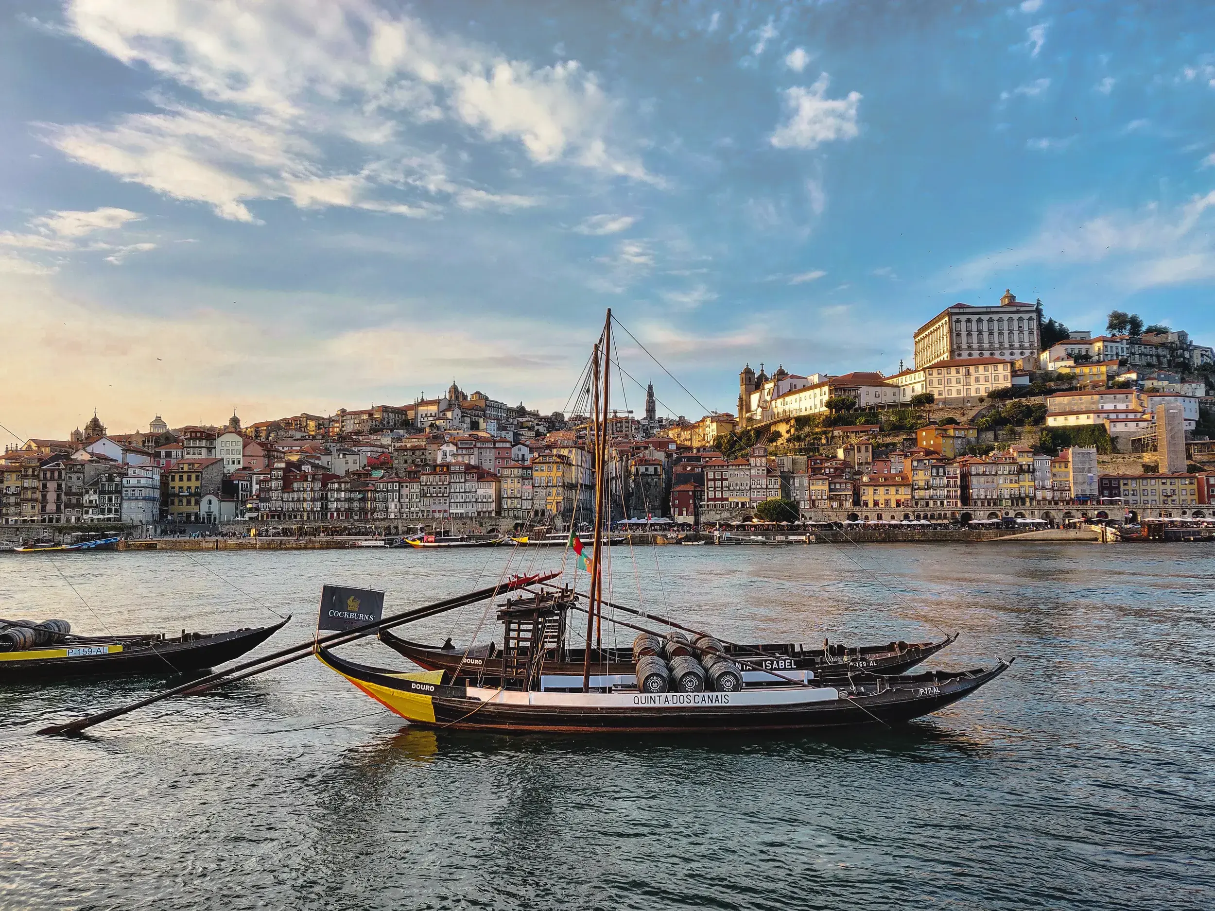 Traditionelle Rabelo-Boote mit Portweinfässern auf dem Douro vor der malerischen Kulisse der Altstadt von Porto bei Sonnenuntergang.